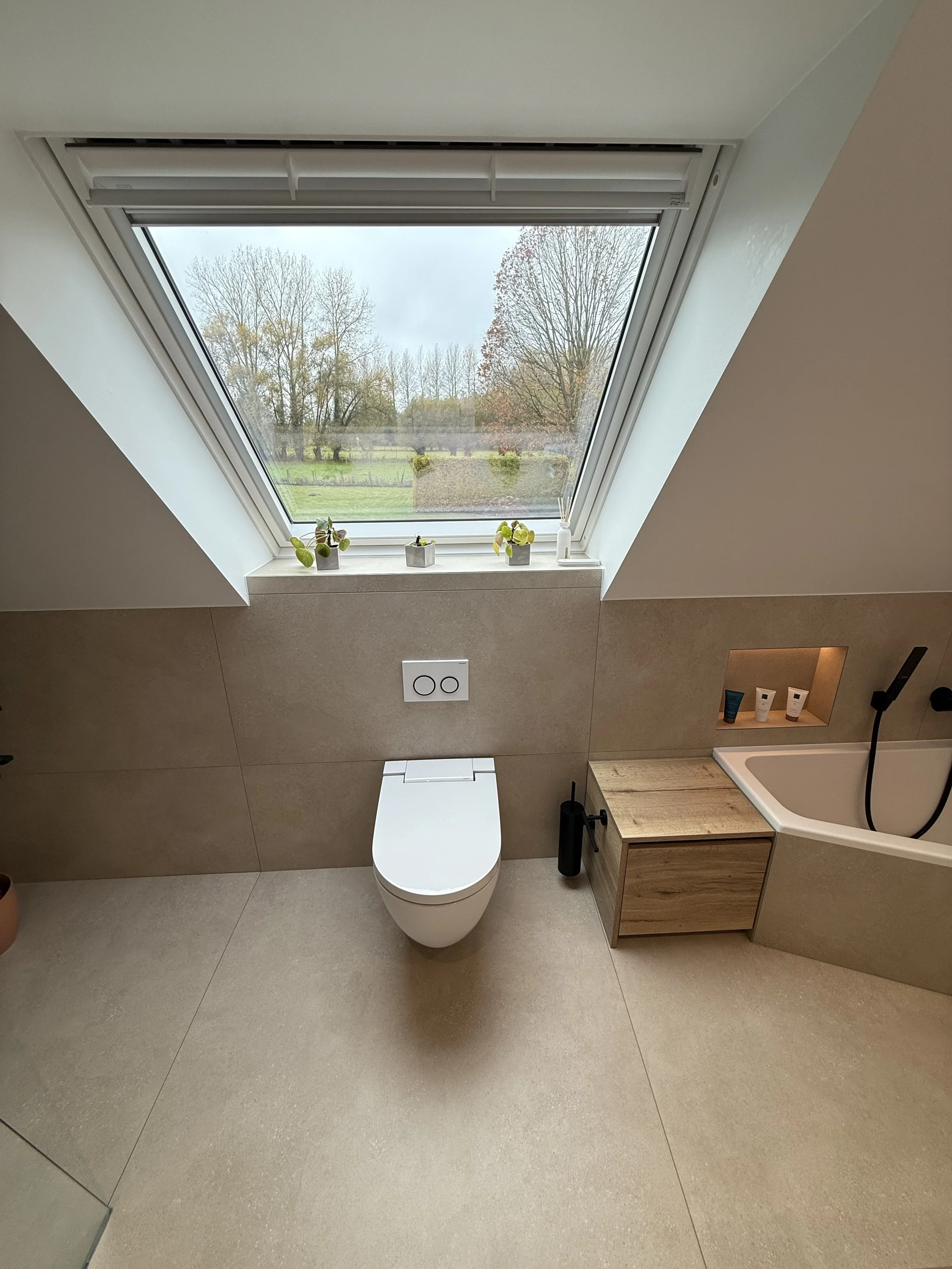 Badkamer met een plafondraam, een renvoirtoliet, een houten kastje en een bloemenvase op het vensterbankje onder het raam.