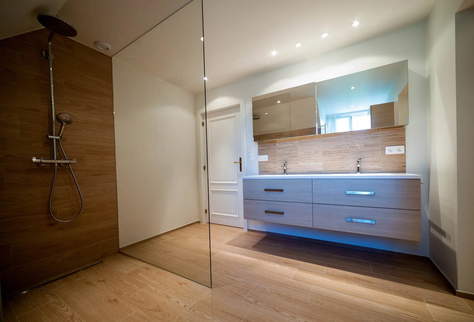 Moderne badkamer met dubbele wastafel, grote spiegel, houten kast, en inloopdouche met houten wand.