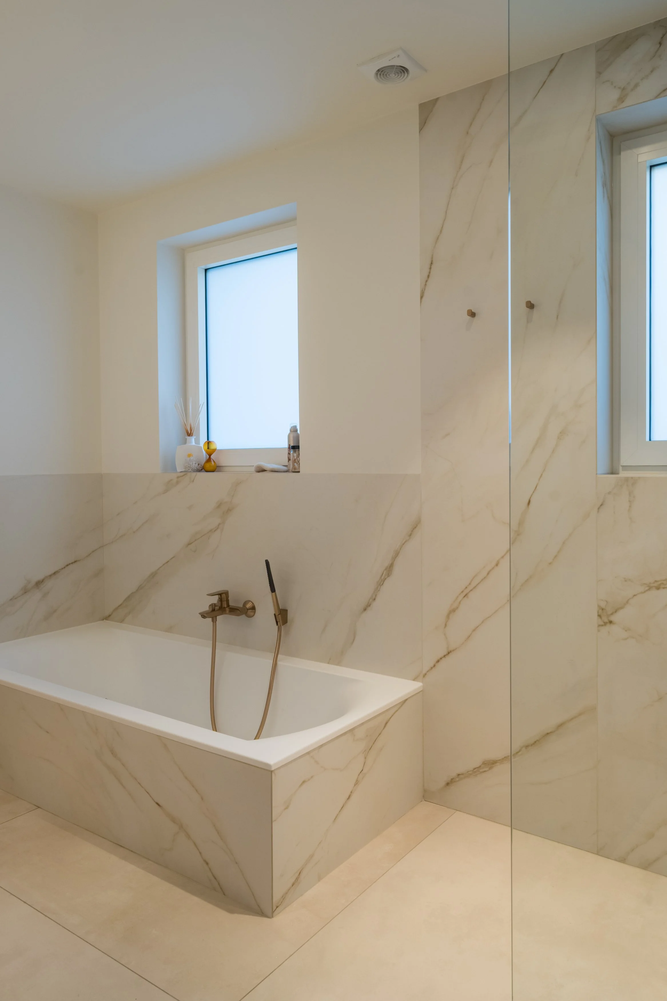 Badkamer met een inbouwbad, marmeren wand en twee ramen.