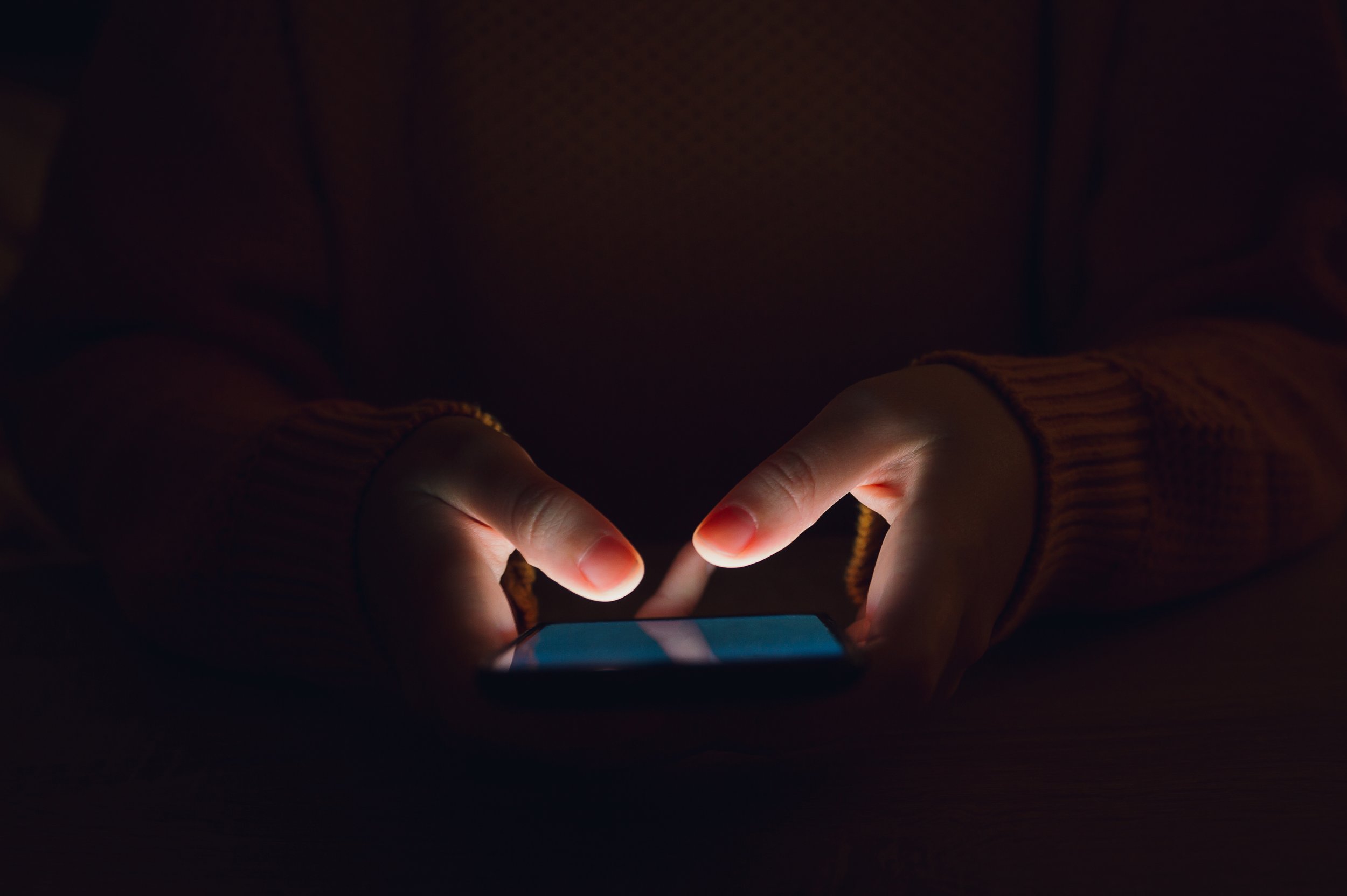 Hands holding a smart phone with a darkened background