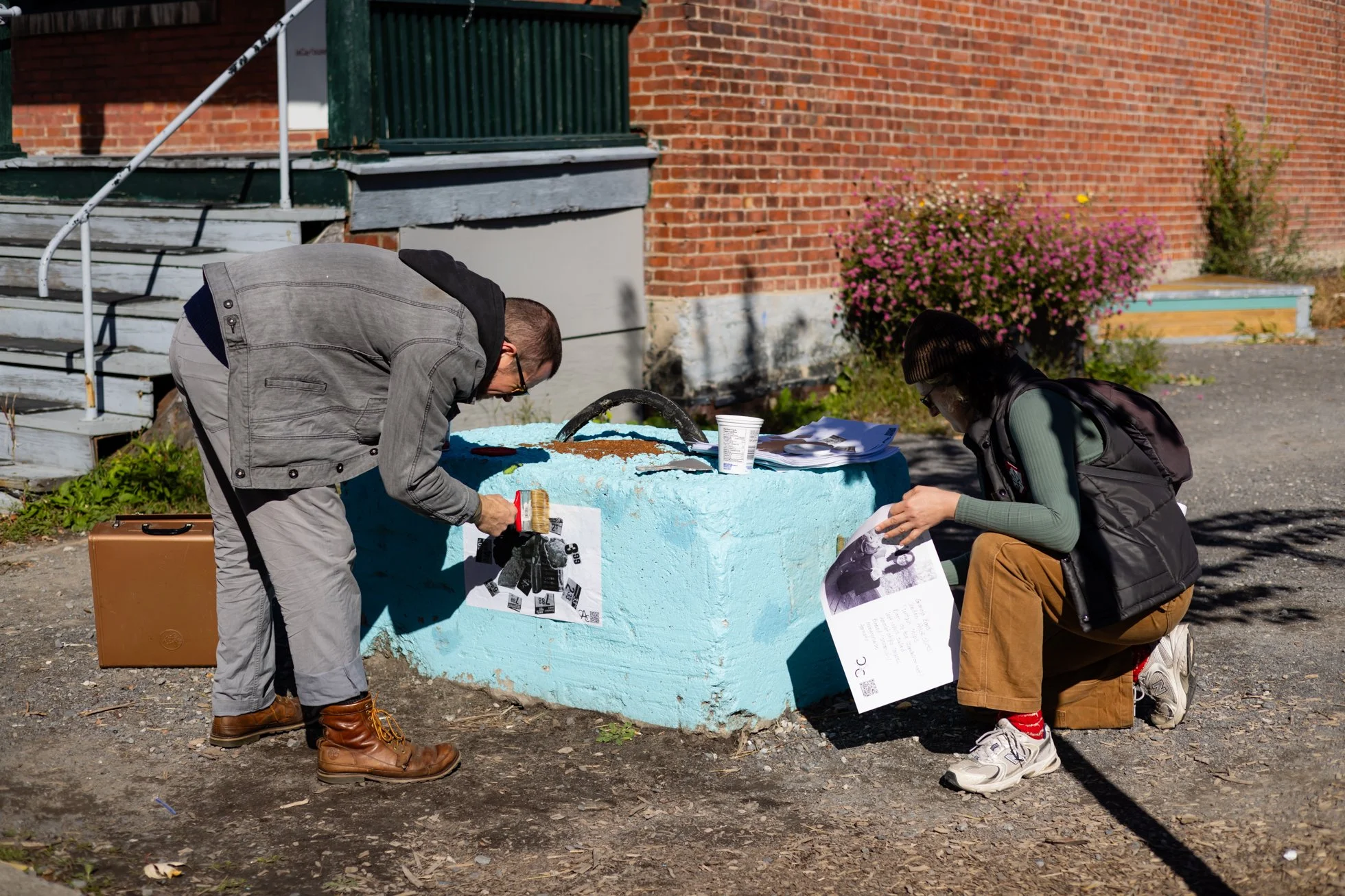 Deux personnes installent une affiche de collage dans l’espace public à Montréal à l’aide de colle de farine dans le cadre du projet Manger, travailler / Food & Labour.