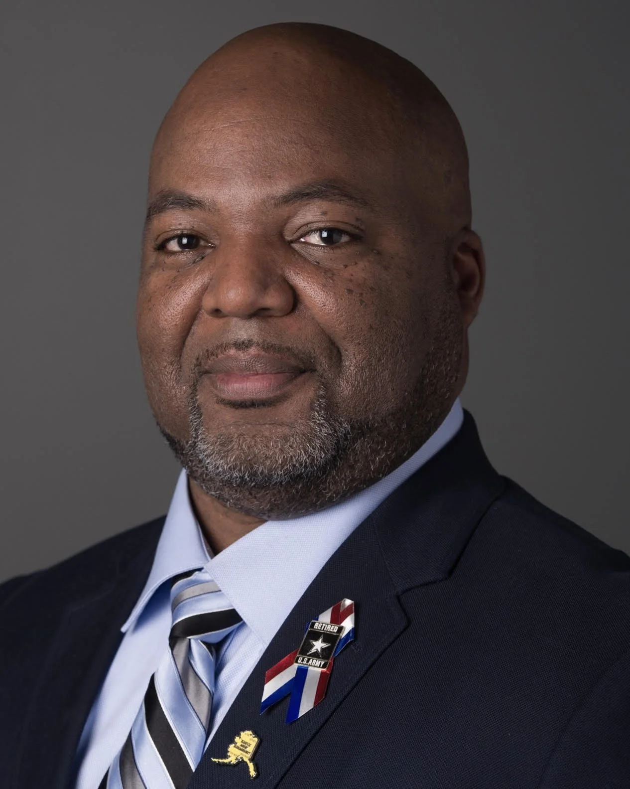 Photo of John, a black middle-aged man wearing a dark suit with a U.S. Army Retired lapel pin