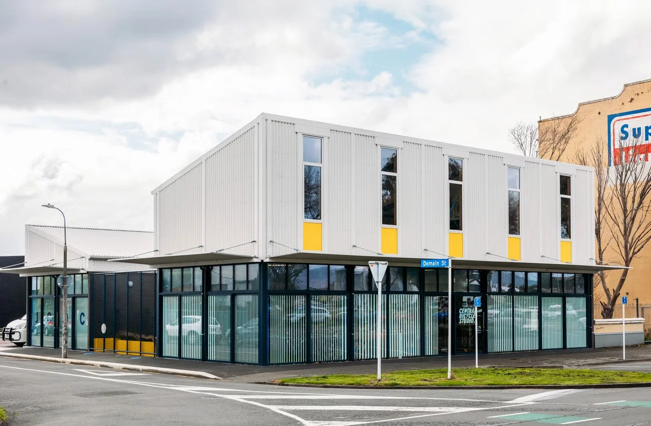 Modern two-story building with a commercial space on the ground floor, city street, parking lot, street signs, and a cloudy sky.