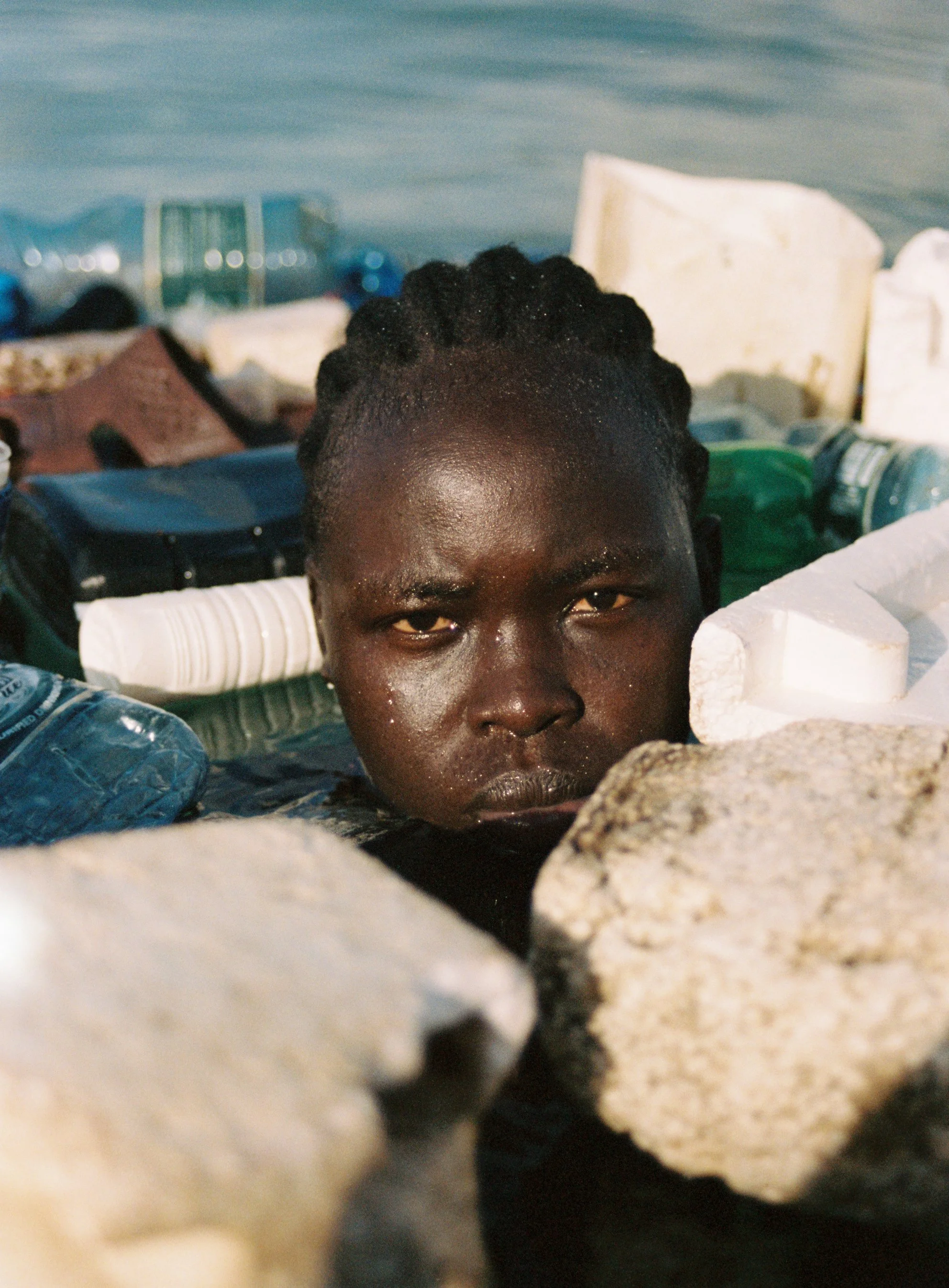 A woman looking disheartened in the ocean with plastic floating around her.