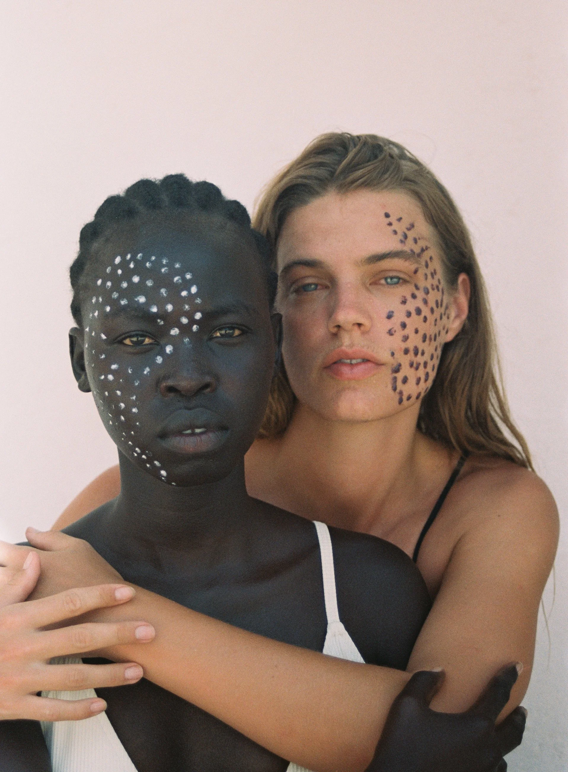 Two women embracing, one with the yin symbol painted on her face and the other with yang.