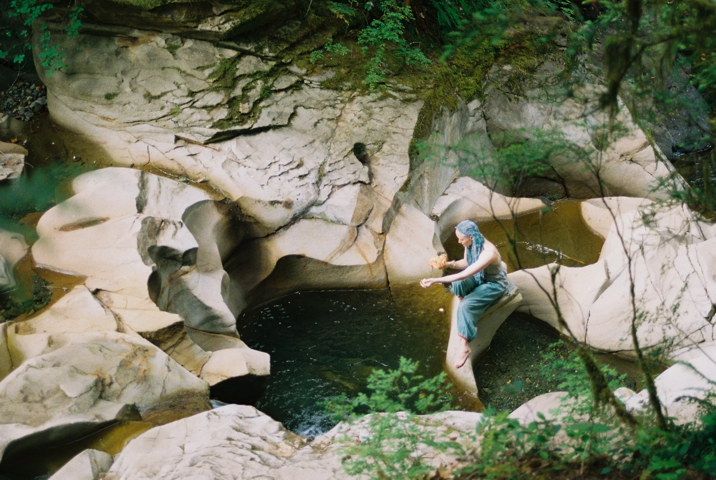 A woman holding a rose at a creek with smooth  sandstone around her.