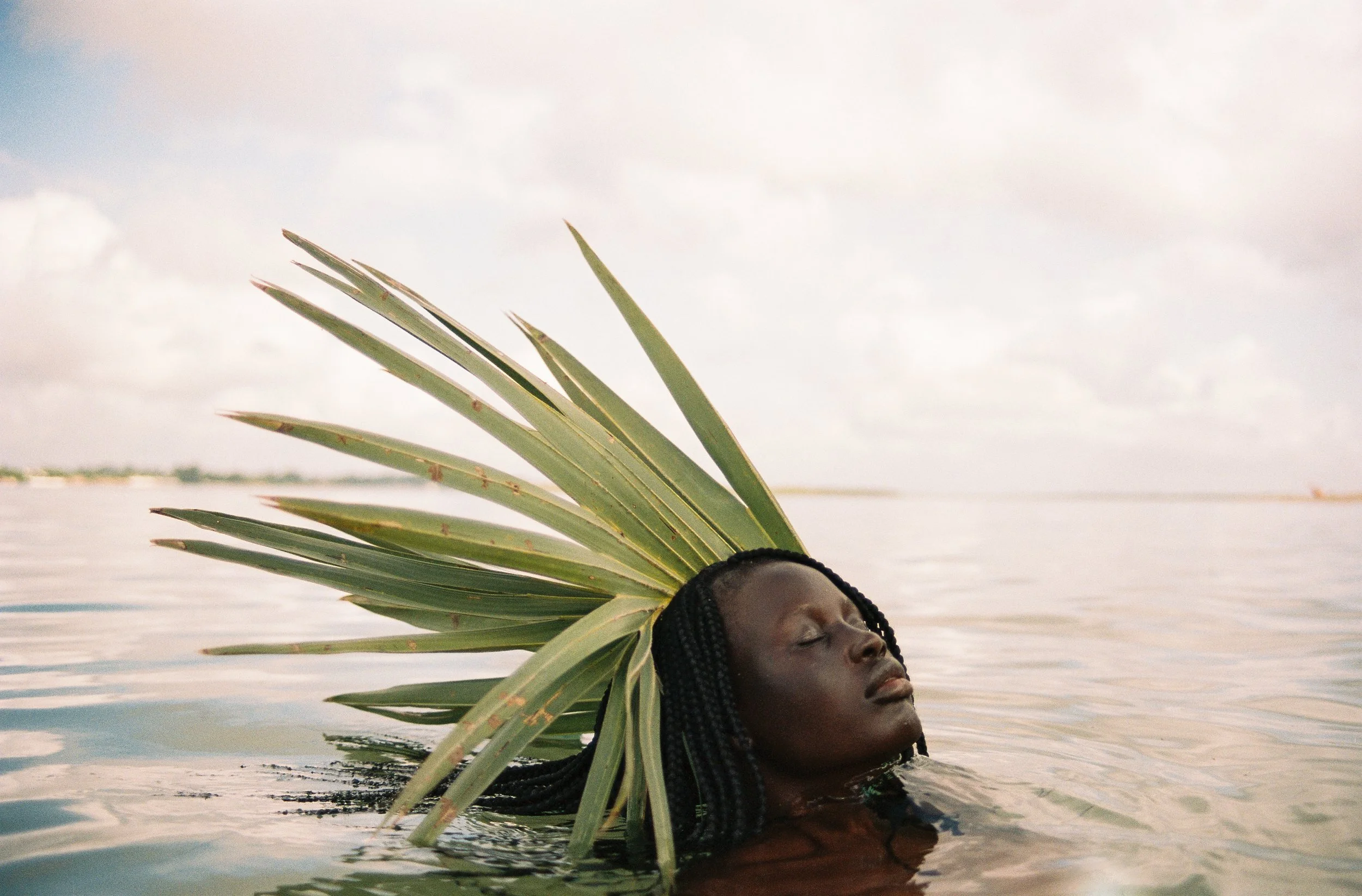 A woman in the water wearing a crown made of palm leaves.