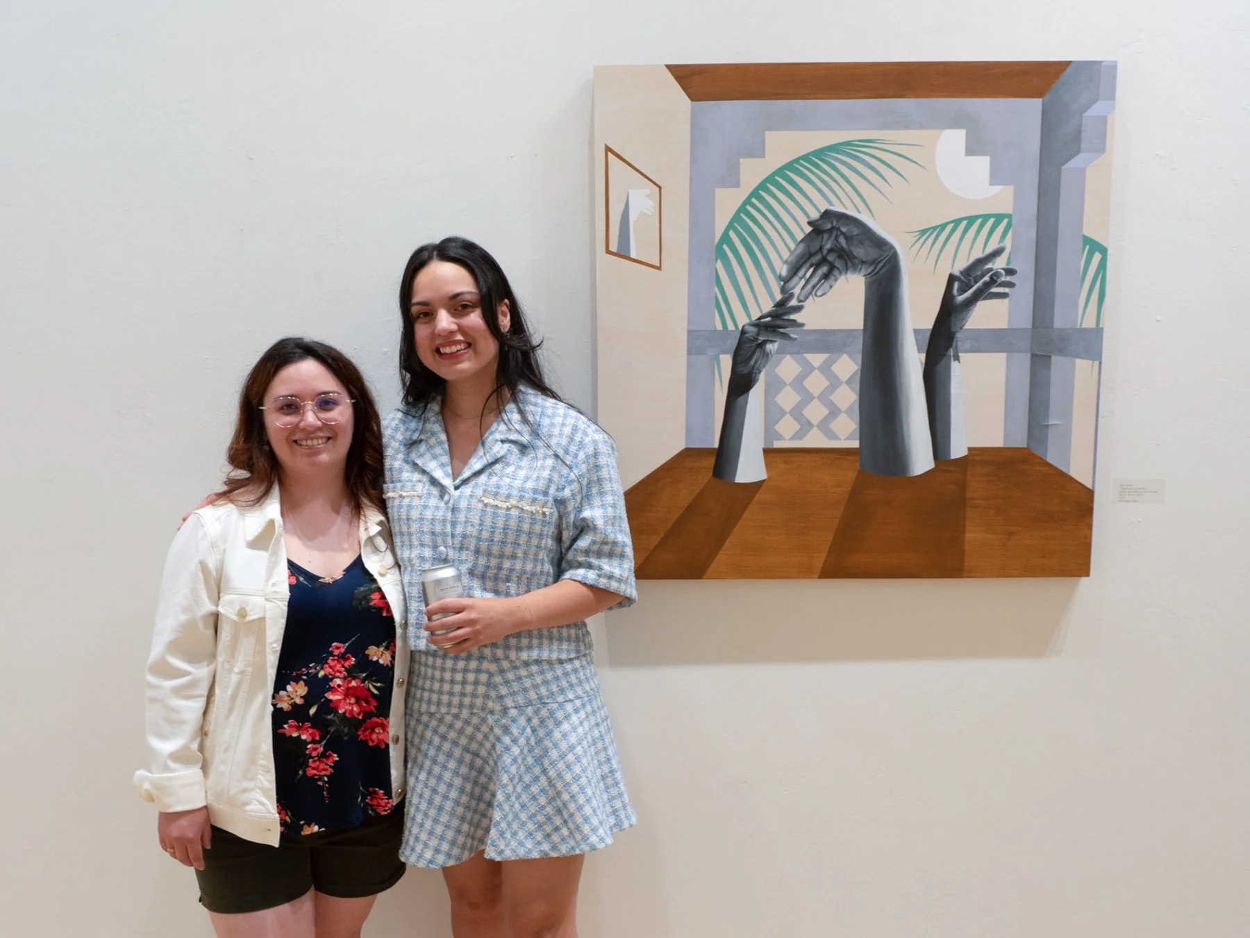 Artist April Werle with sister at the opening of Halo-Halo: The Mixed Children, 2023, standing beside "I belong to my family." — grayscale hands reaching in a tropical interior with palm fronds and diamond tile.