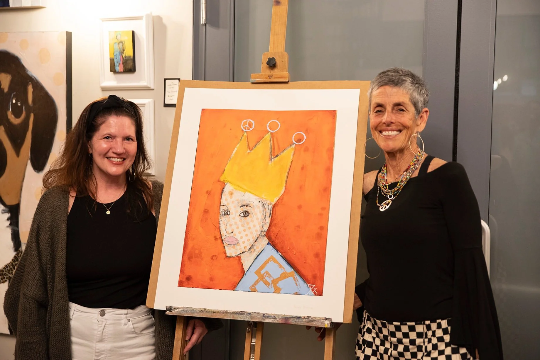 photograph of artist Renee Broxson with Jennifer Steele of Cultural Arts Alliance of Walton County standing on either side of a giclee print of "Crowned in Courage" at Distillery 98 in Santa Rosa Beach, FL, in April 2026