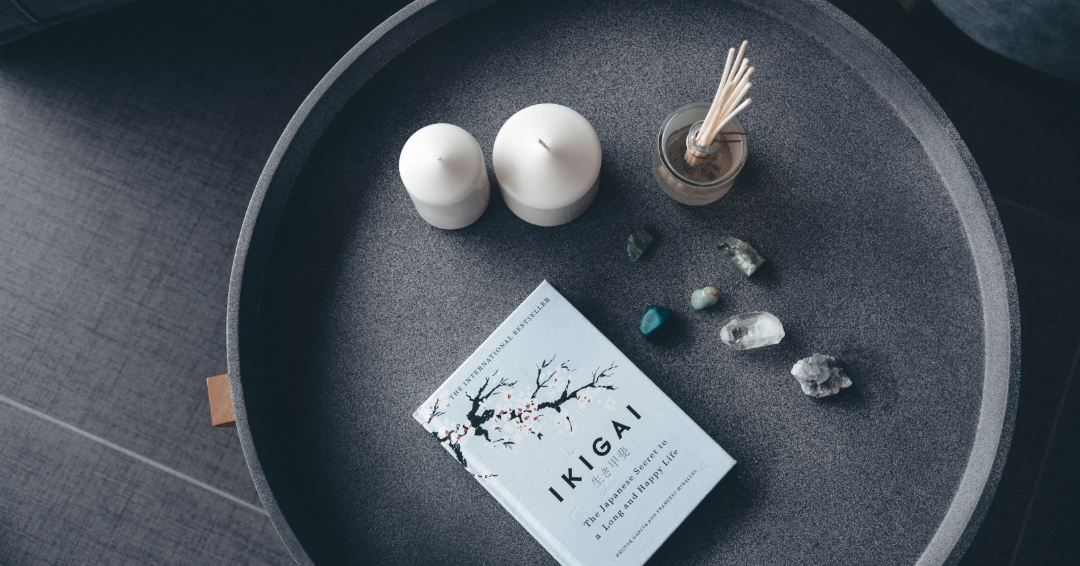 photograph of the book, IKIGAI, laying on top of a gray tray next to candles, rocks and incense. The tray is laying on top of a gray surface