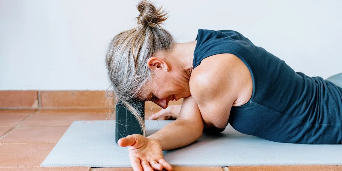 A woman uses a yoga block for a supported floor stretch, representing static flexibility work explained in Dynamic Stretches vs Static Stretches.
