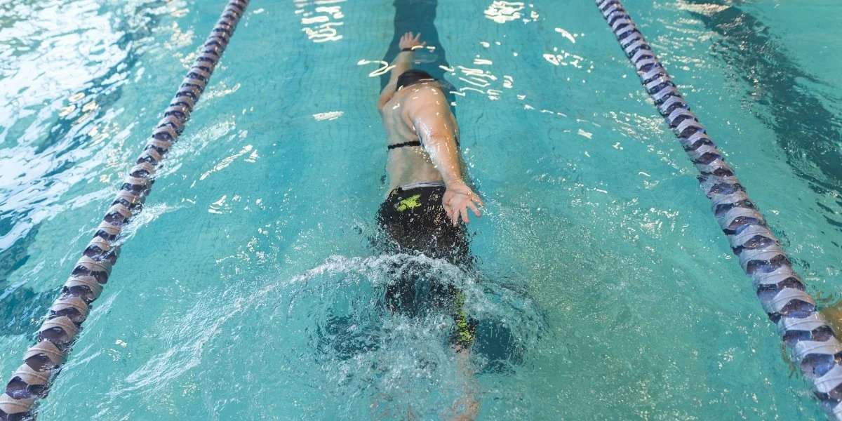 A swimmer moves at a steady pace in a pool, demonstrating what is active recovery through low-impact cardiovascular exercise.