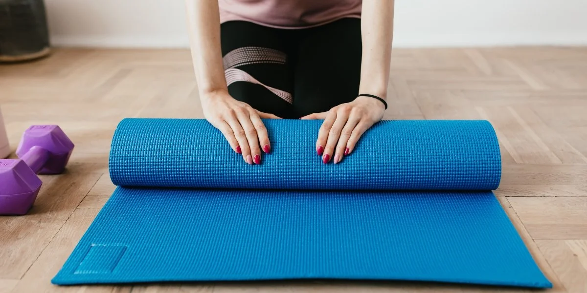 A person rolling out a yoga mat indoors, preparing for gentle movement that supports the best active recovery workouts on a rest day.