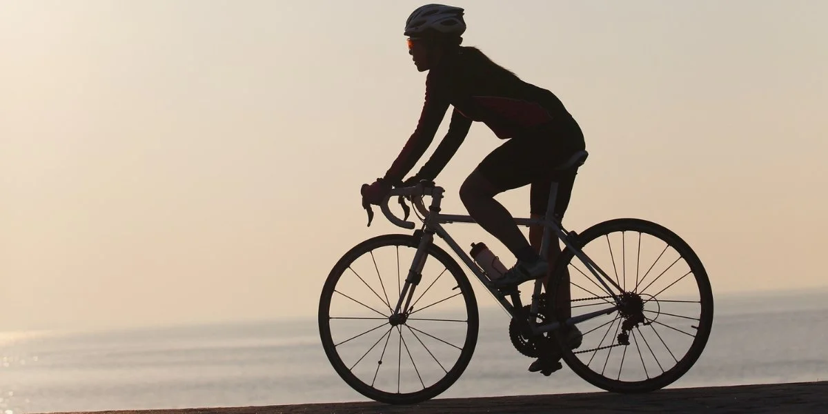 A cyclist rides calmly along a path at sunset, showing what is active recovery through light cycling and movement.