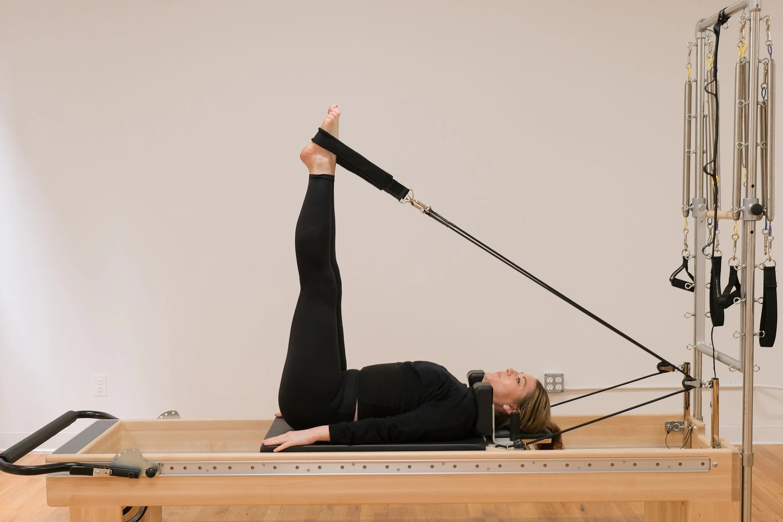Client performing a supported leg press on a reformer to improve bone loading and control during Pilates