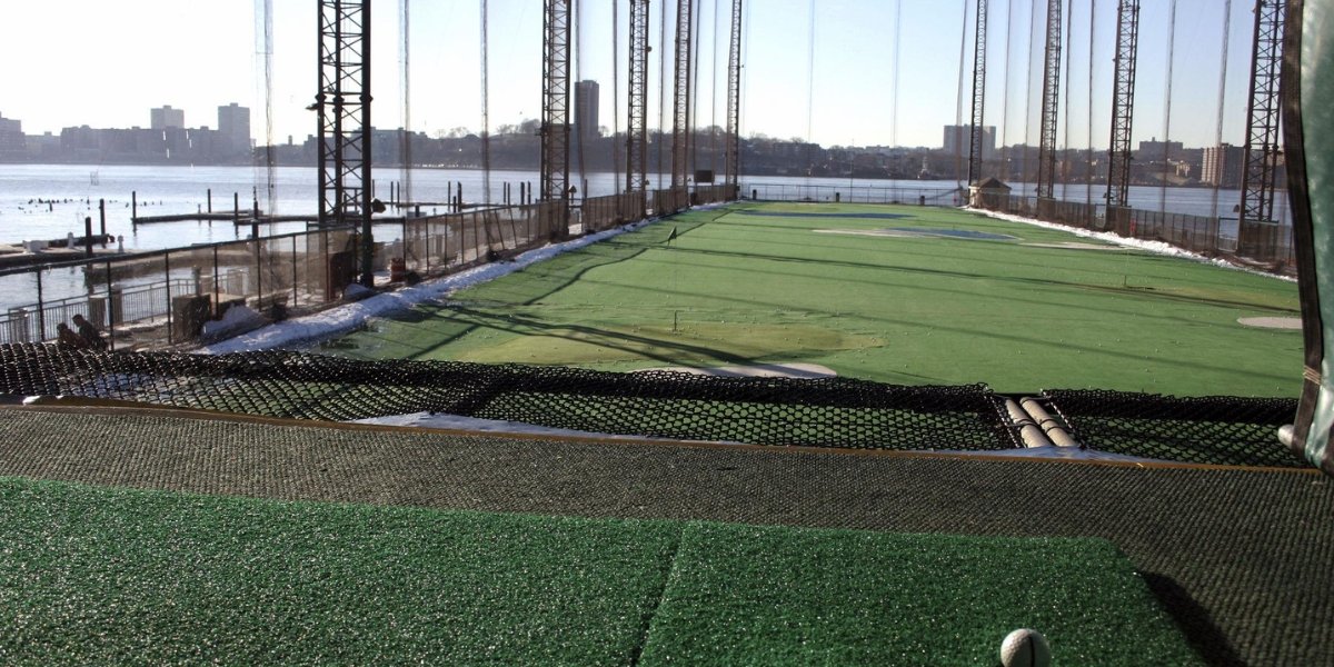 Chelsea Piers golf practice facility featuring artificial turf driving ranges with Hudson River and Manhattan waterfront views, demonstrating Chelsea Piers activities including golf instruction and practice with scenic backdrops.