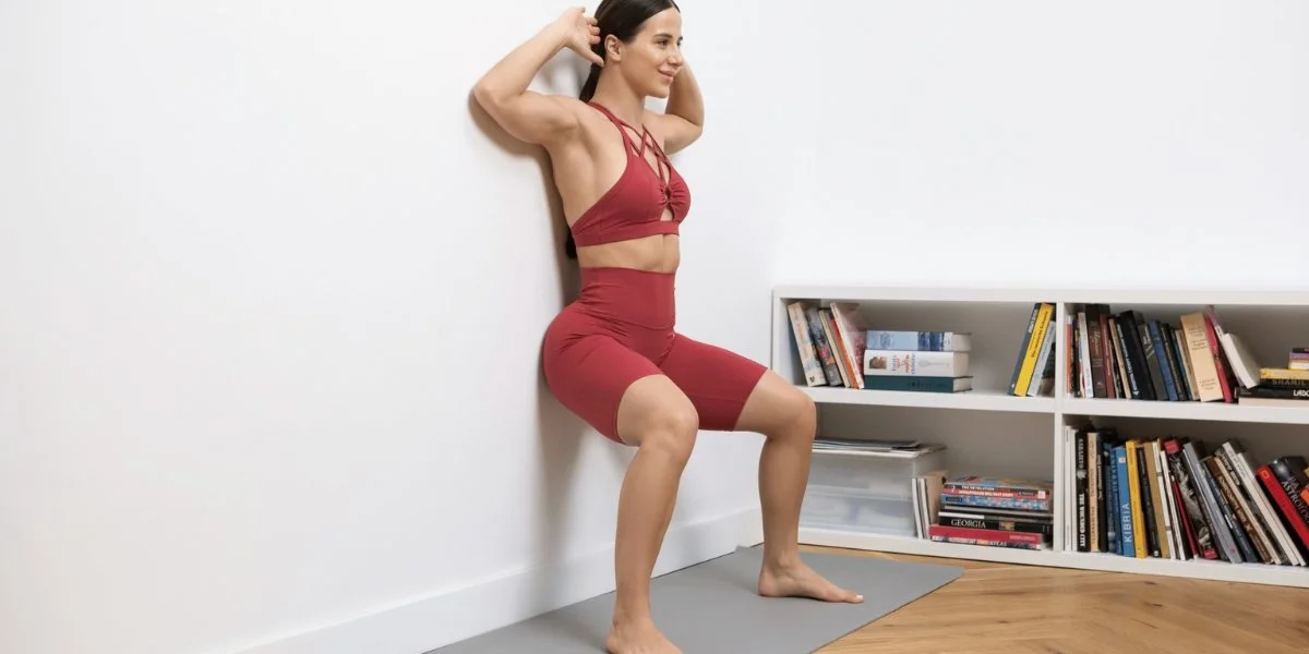 Woman performing wall angels exercise with her back against a white wall, demonstrating proper shoulder mobility and posture alignment in a home living space