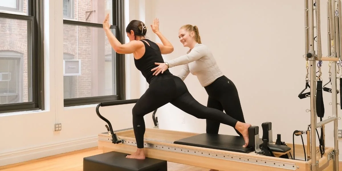 Pilates instructor supports a client performing a standing Reformer lunge in Manhattan, showing why exercise needs vary between individuals.