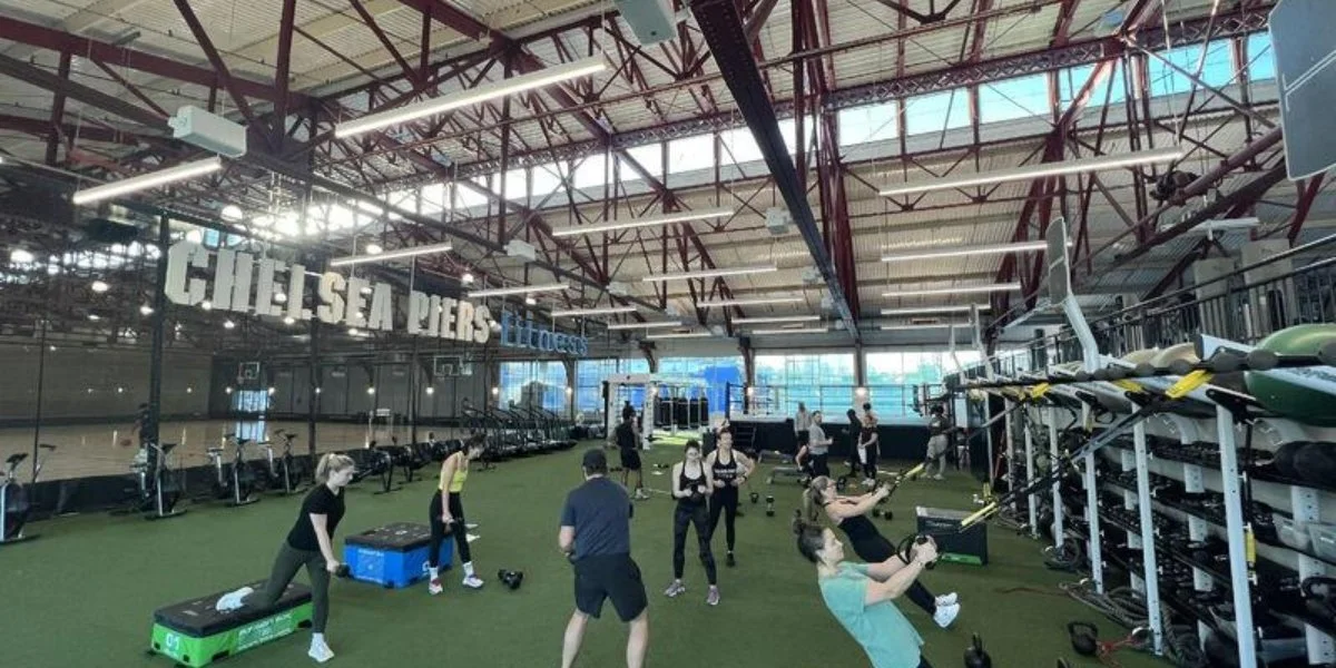 Chelsea Piers Field House drop-in fitness class showing participants exercising on artificial turf with equipment and signage visible, demonstrating Chelsea Piers activities for group fitness training and athletic instruction.