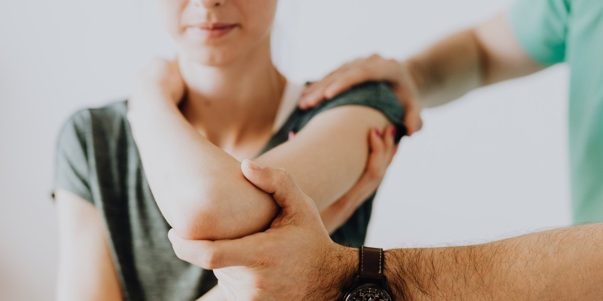 A physical therapist supports a woman’s arm to demonstrate assisted stretching, illustrating passive movement in the context of Active vs Passive Range Of Motion Exercises.