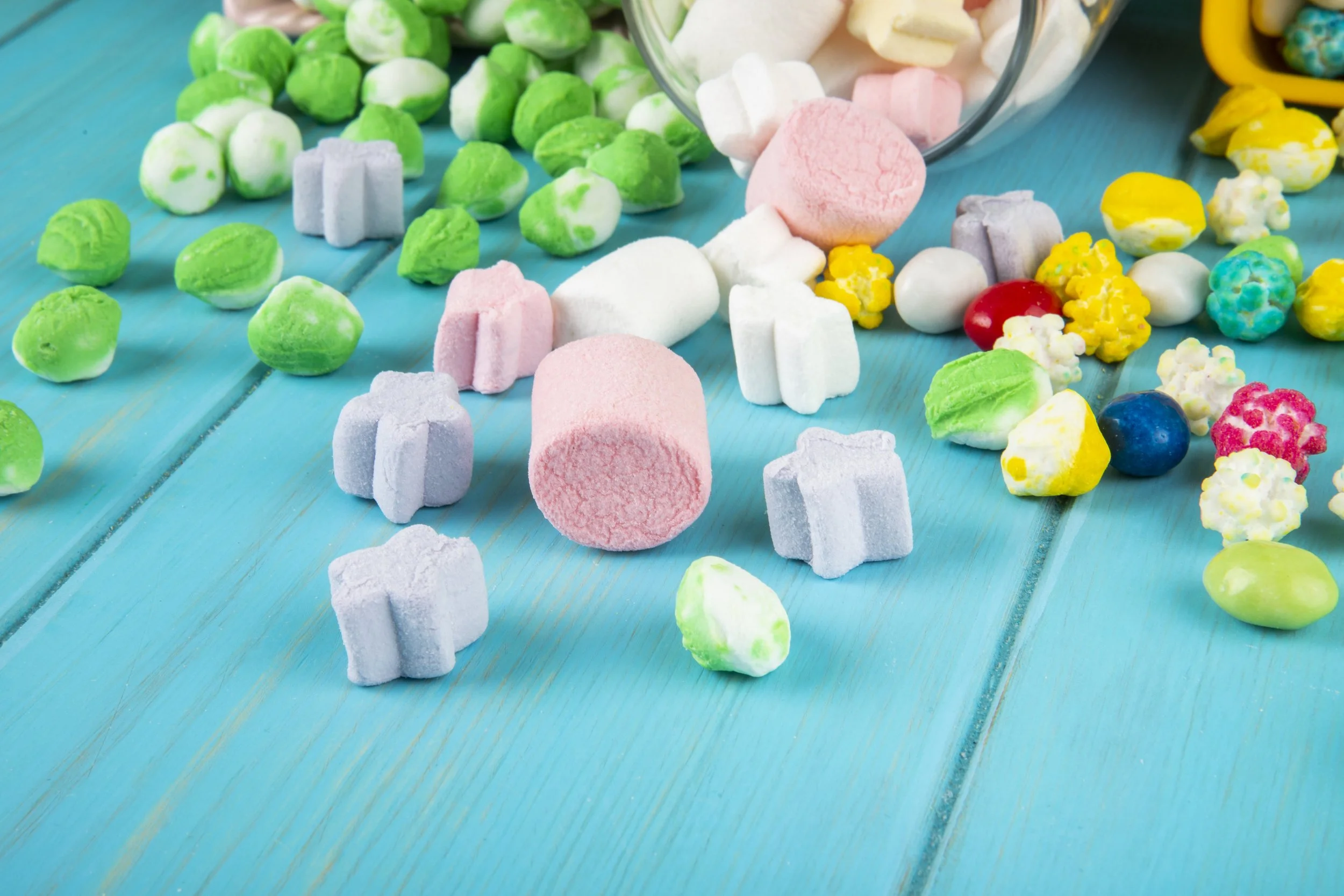 side-view-various-colorful-candies-marshmallow-scattered-from-glass-jar-blue-background.jpg