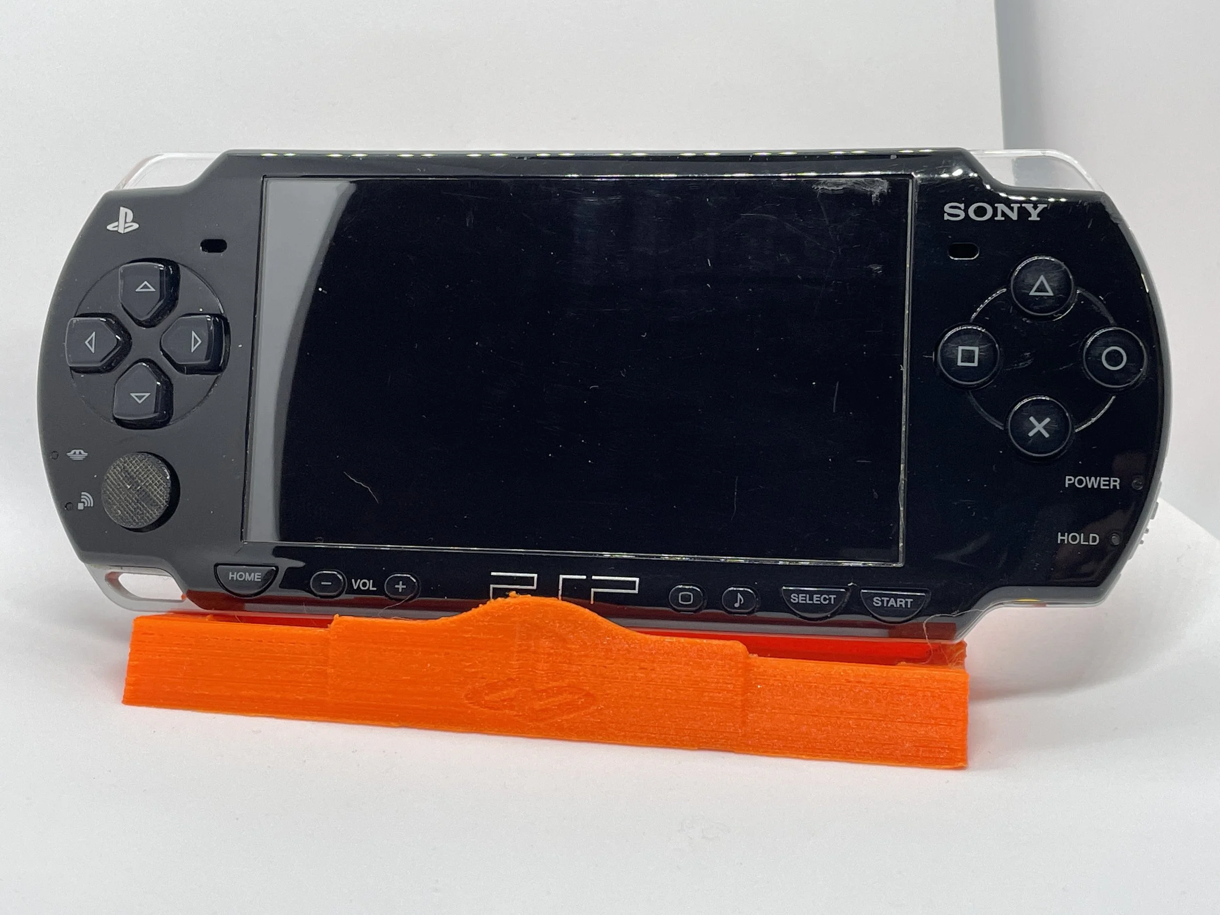 A black Sony PlayStation Portable (PSP) handheld gaming console resting on a orange stand.