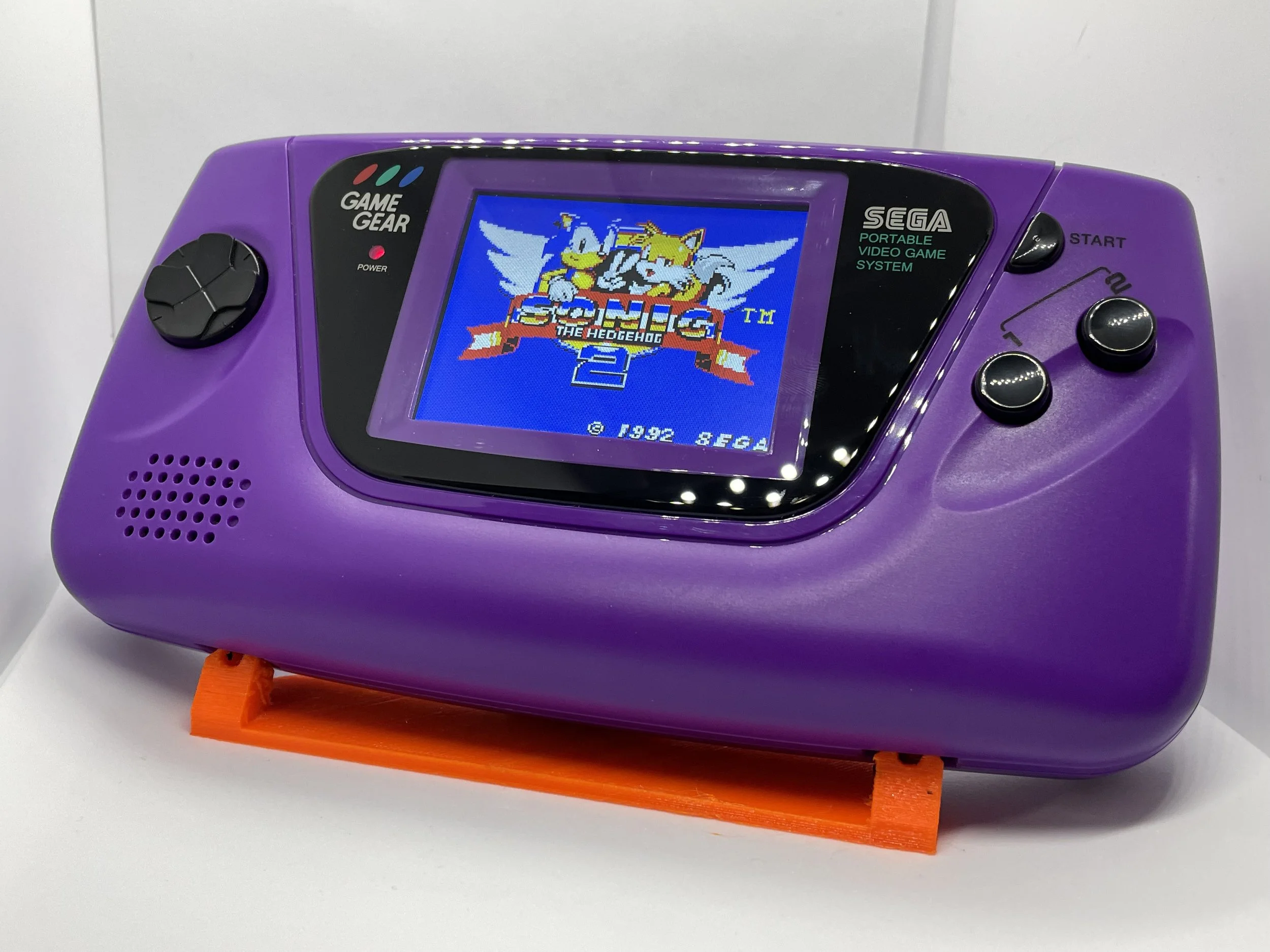 A purple Sega Game Gear portable handheld gaming device with the Sonic the Hedgehog 2 game displayed on the screen.