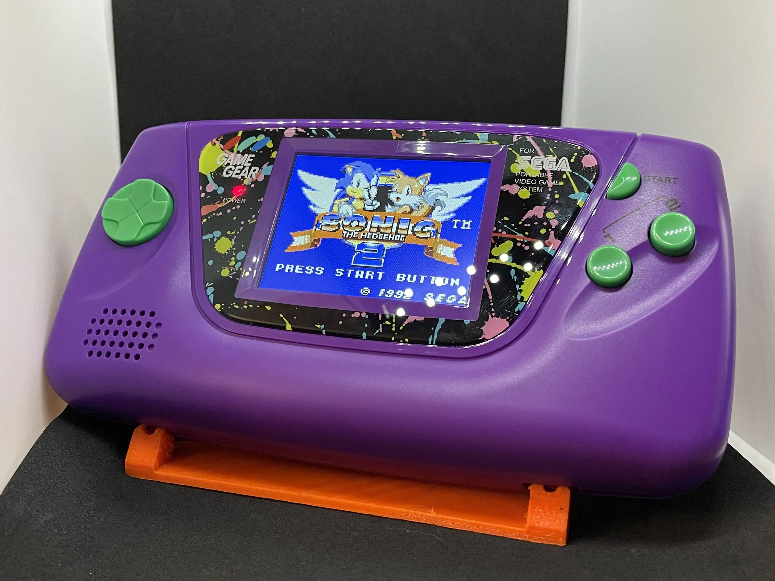 A purple handheld gaming console with green buttons, displaying the title screen of Sonic Adventure for the Sega Game Gear from 1999.