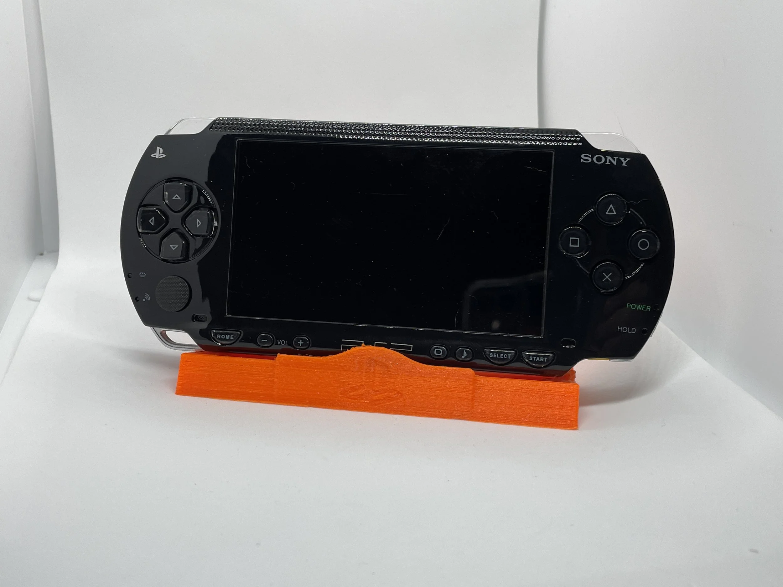 A black Sony handheld gaming console resting on an orange stand on a white surface.