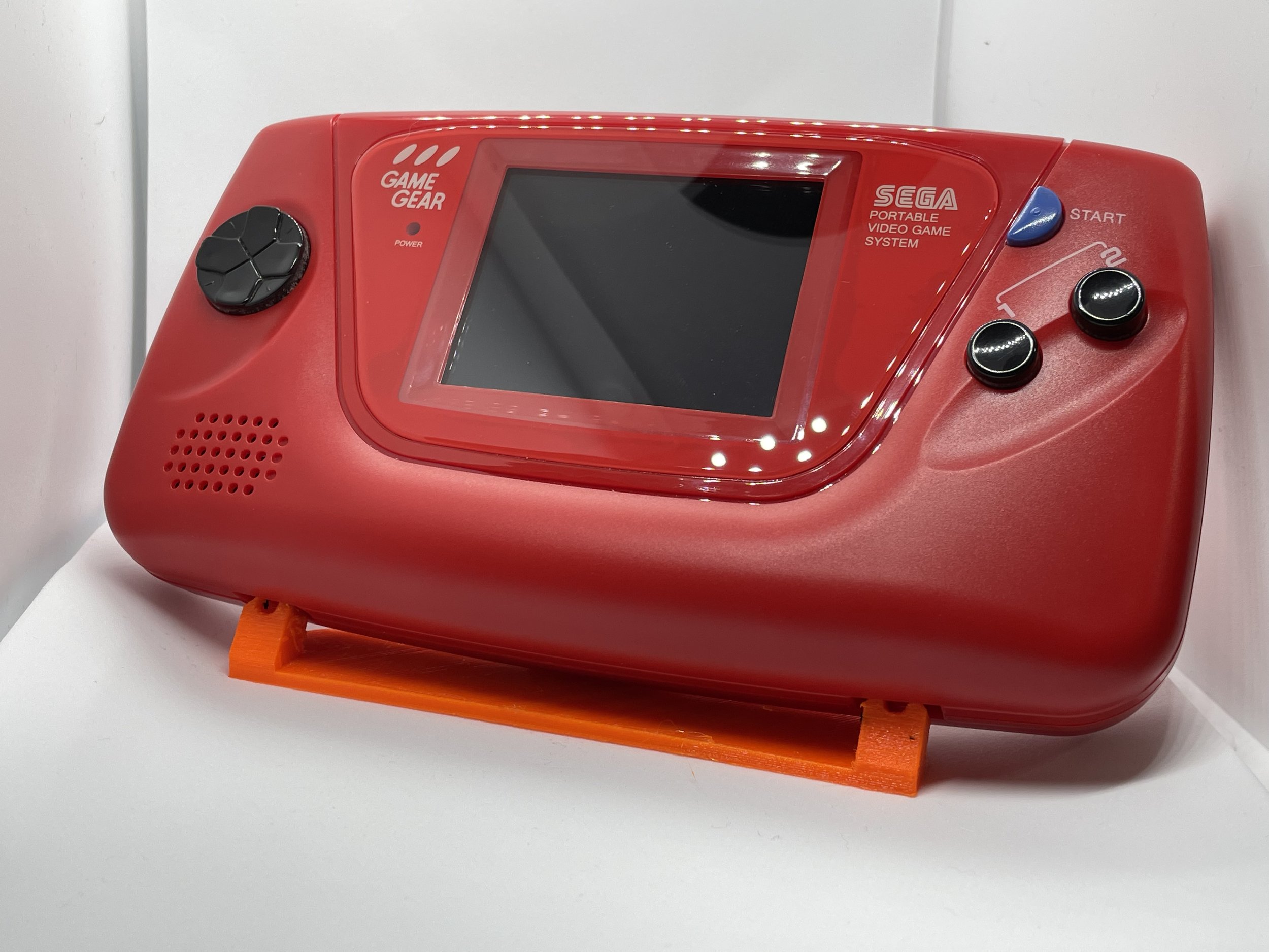 Red Sega Game Gear portable video game system with a black control pad on the left, two black buttons on the right, and a large screen in the center.