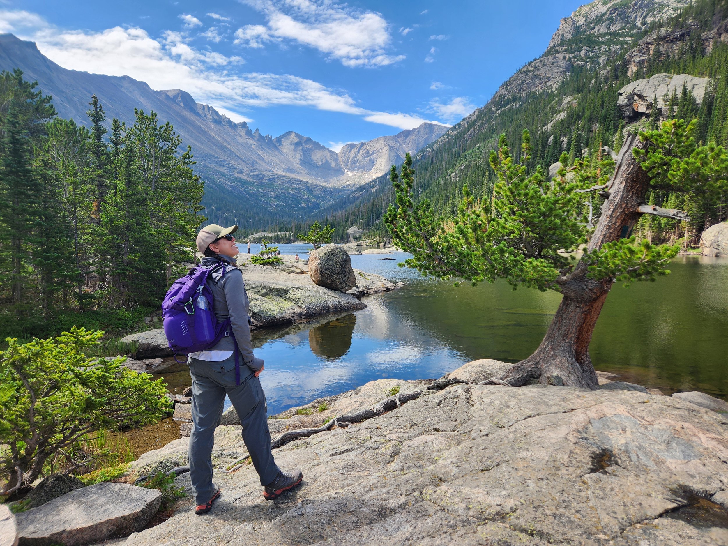 Femme Trek guest standing next to Mills Lake with the Continental Divide in the background on a women-only guided hiking tour with Femme Trek in Rocky Mountain National Park