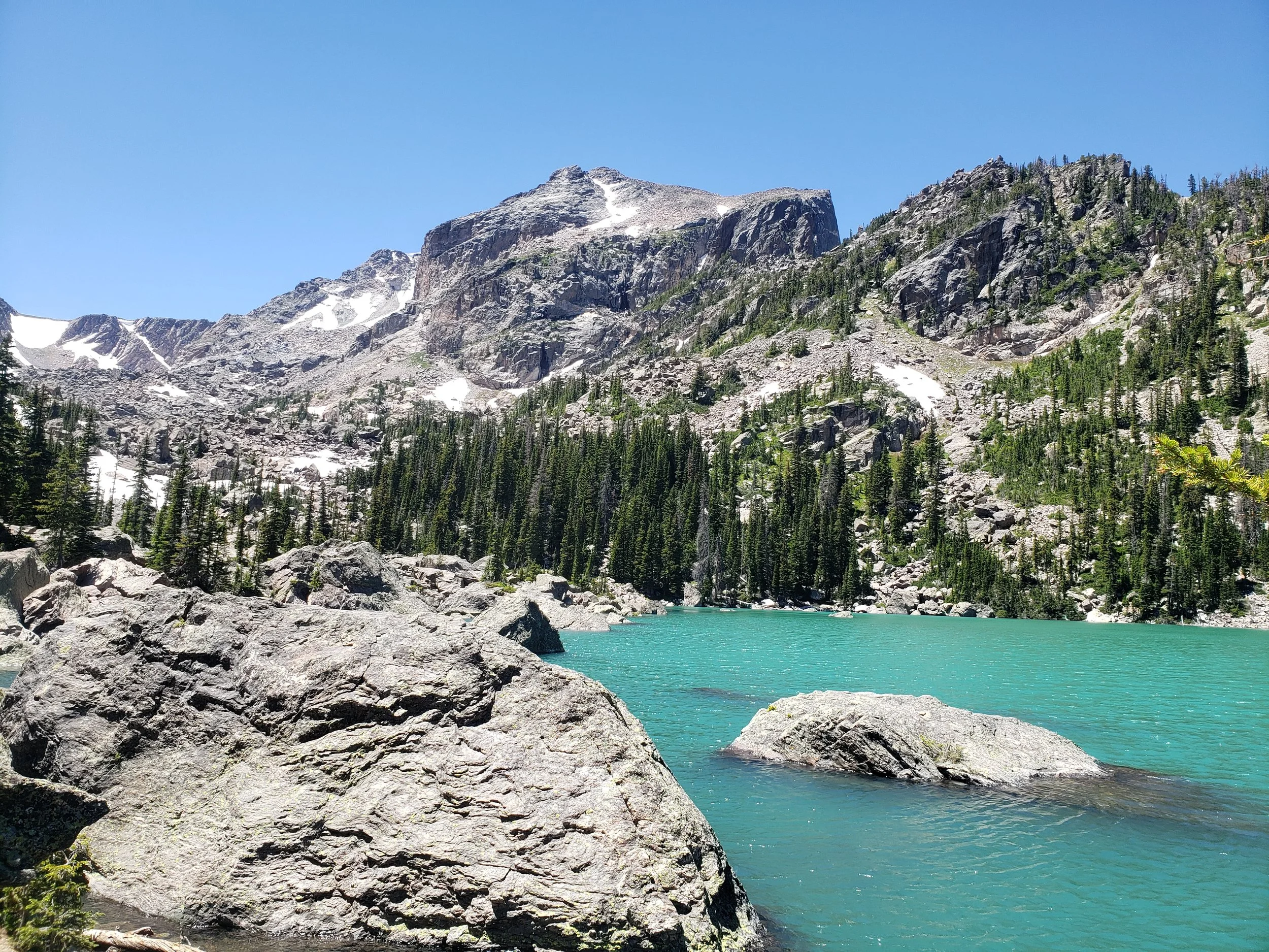 Brilliant turquoise waters of lake haiyaha are pictures along with giant granite boulders surrounding the lake and Hallett Peak and the Continental Divide in the background.
