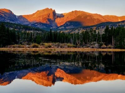 The mountains of the Continental Divide glow red with the mountains reflected in Sprague Lake on a women-only guided hiking tour in Rocky Mountain National Park with Femme Trek