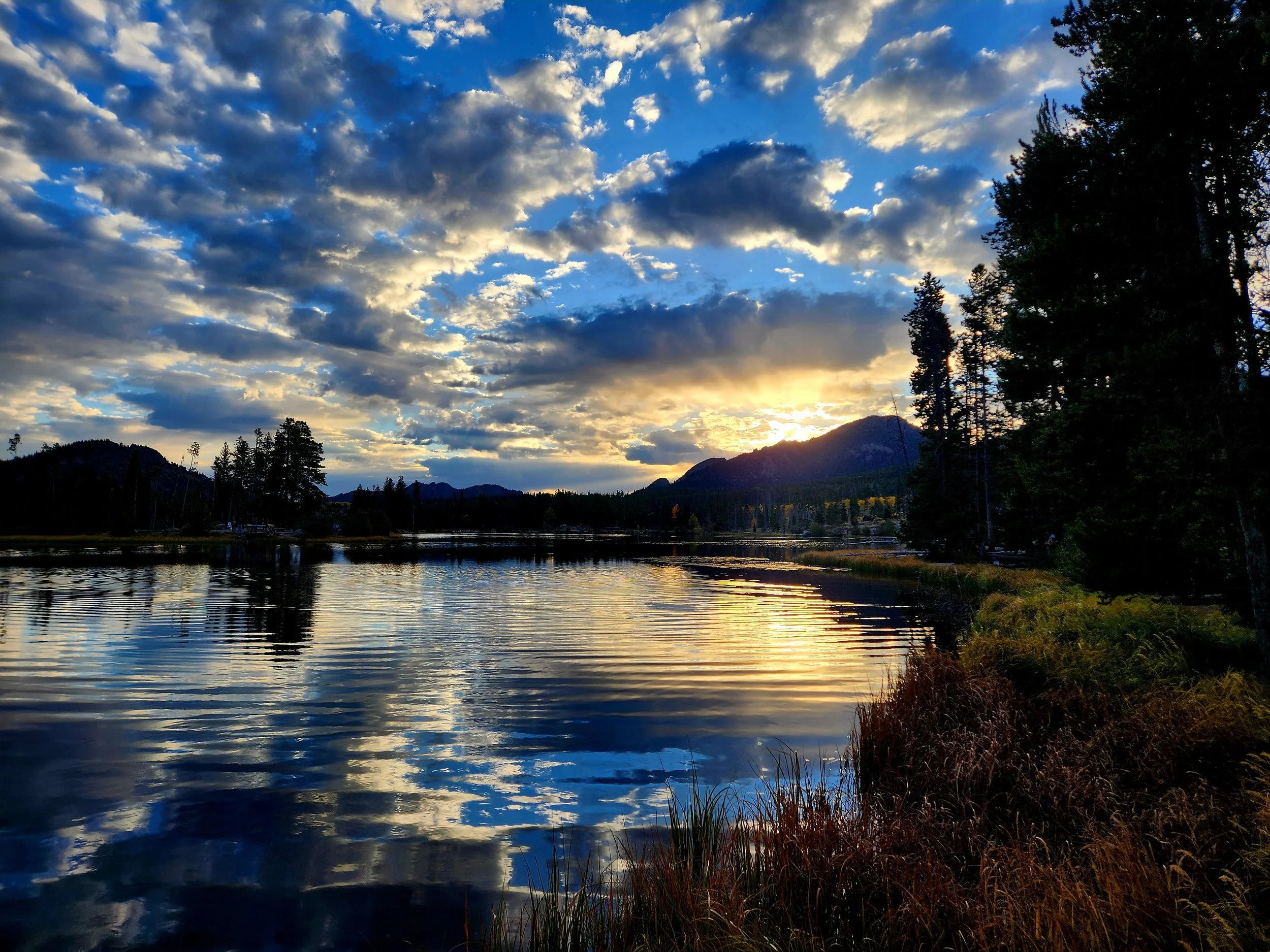 Woman watching a sunrise over a mountain lake on a guided hiking tour for women with Femme Trek in Rocky Mountain National Park, Colorado.