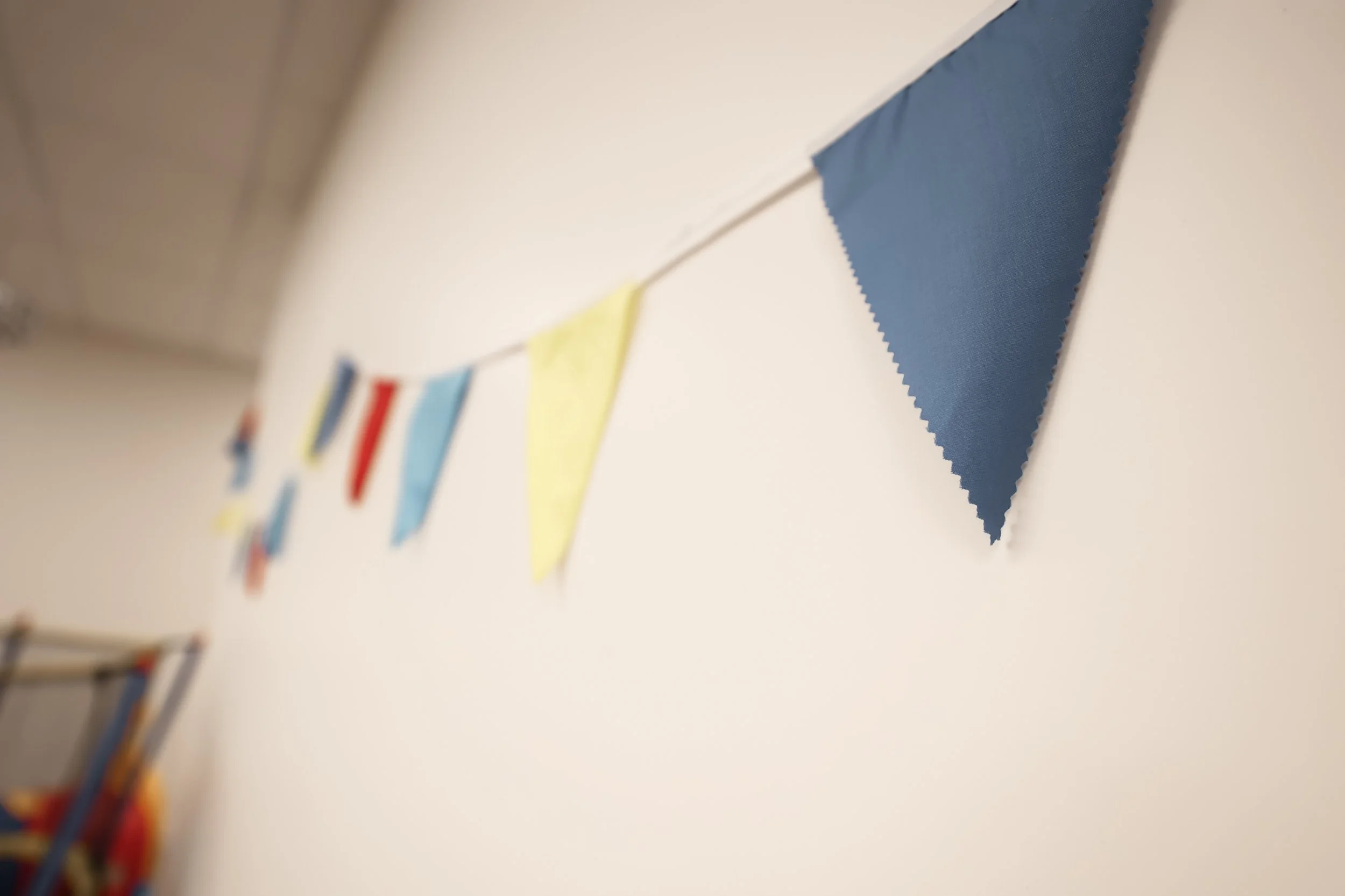 Colorful fabric pennant banner hanging on a wall, with flags in blue, yellow, red, and other colors.
