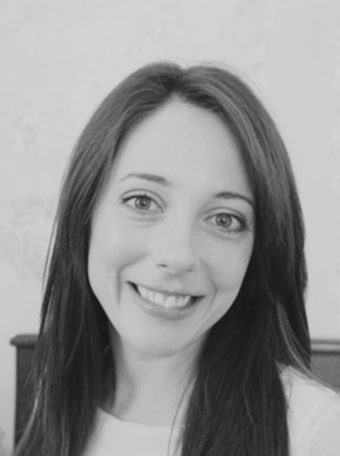 A black and white portrait of a woman with straight, shoulder-length hair, smiling shown from the shoulders up.