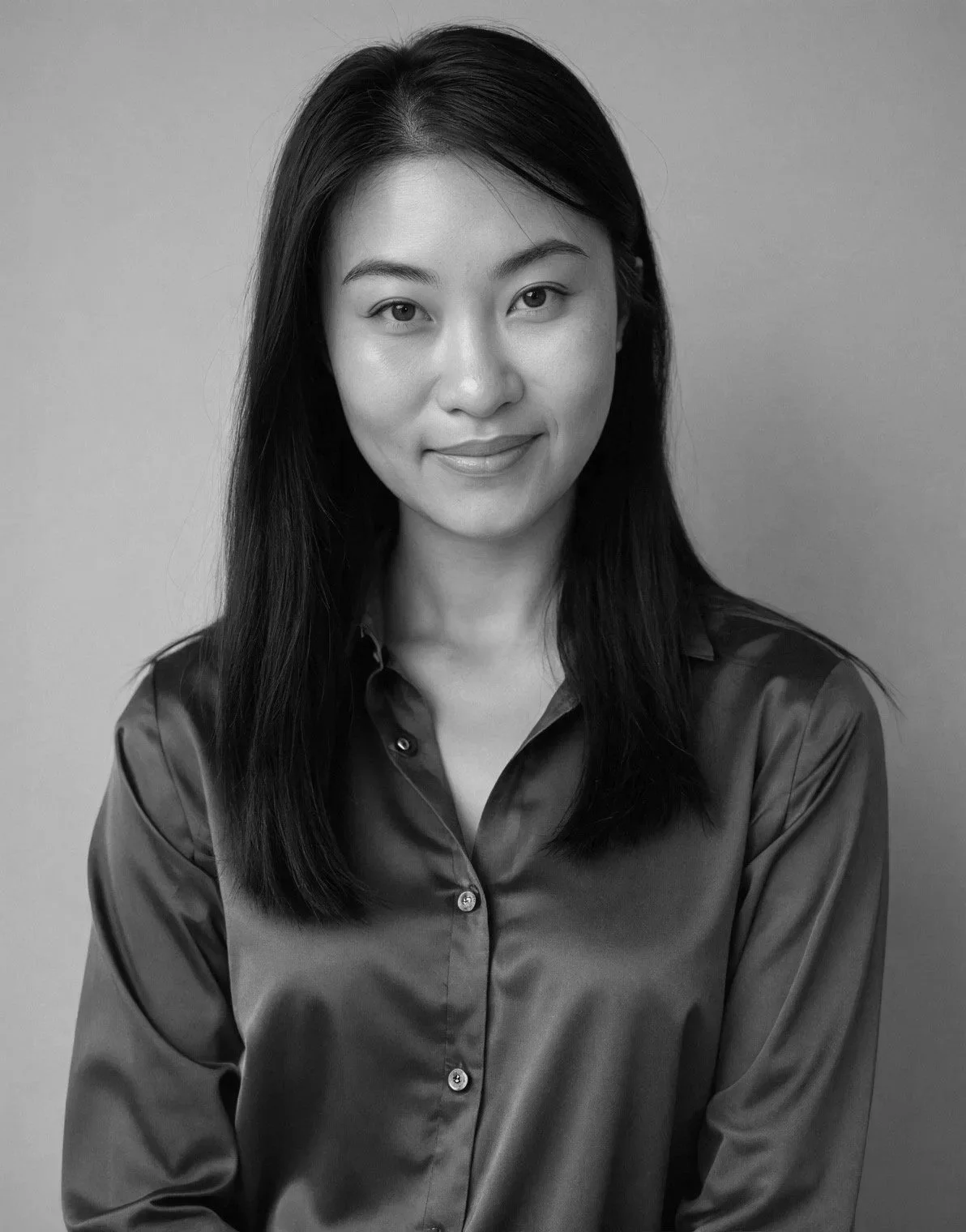 Black and white portrait of a woman with shoulder-length hair, wearing a shiny blouse, smiling slightly, against a plain background.