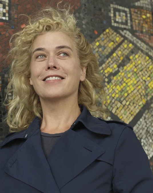 Porträtt av konstnärern Rita McBride. En konstnär med ljust lockigt hår och iklädd dubbelknäpp kavaj.