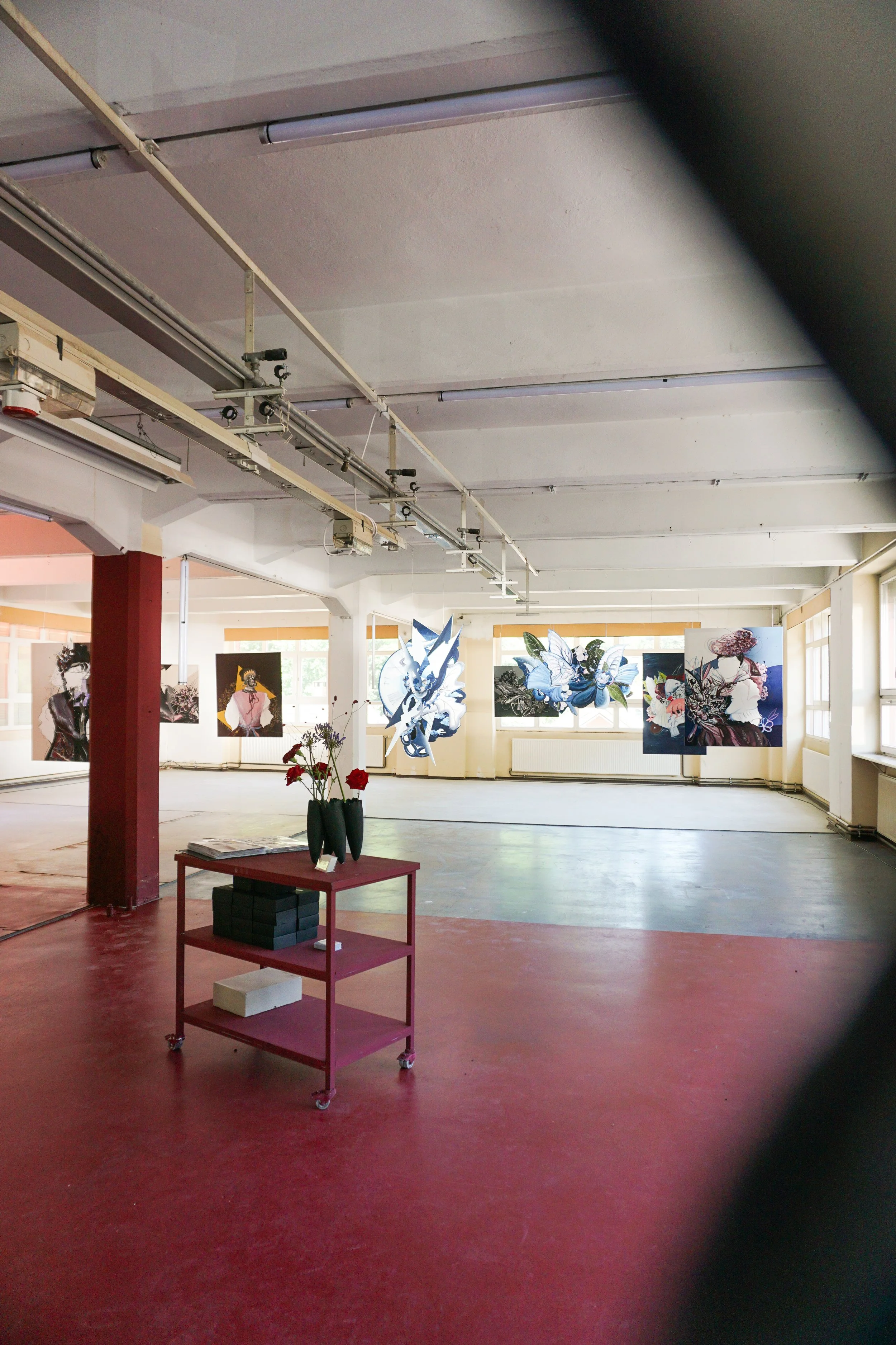 Ein Ausstellungsraum & Kunstgalerie im Schwarzwald des Künstlers José Schloss. mit mehreren Kunstwerken an den Wänden, eine rote Trittleiste mit Vasen und Dekorationen im Mittelpunkt, helle Fenster im Hintergrund, auf dem roten Boden.