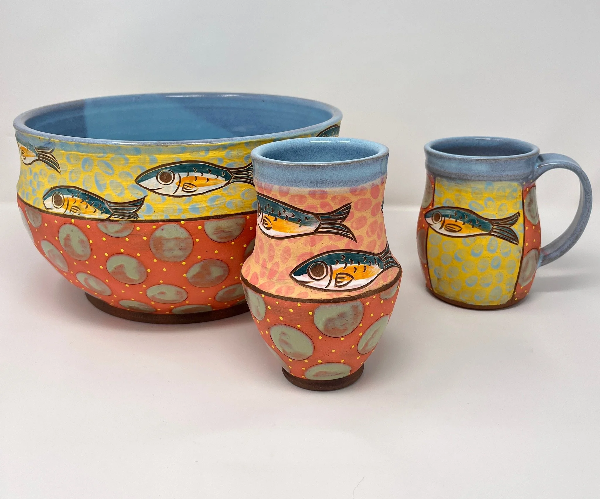 Three colorful ceramic cups with painted fish design, arranged on a white surface against a plain background.