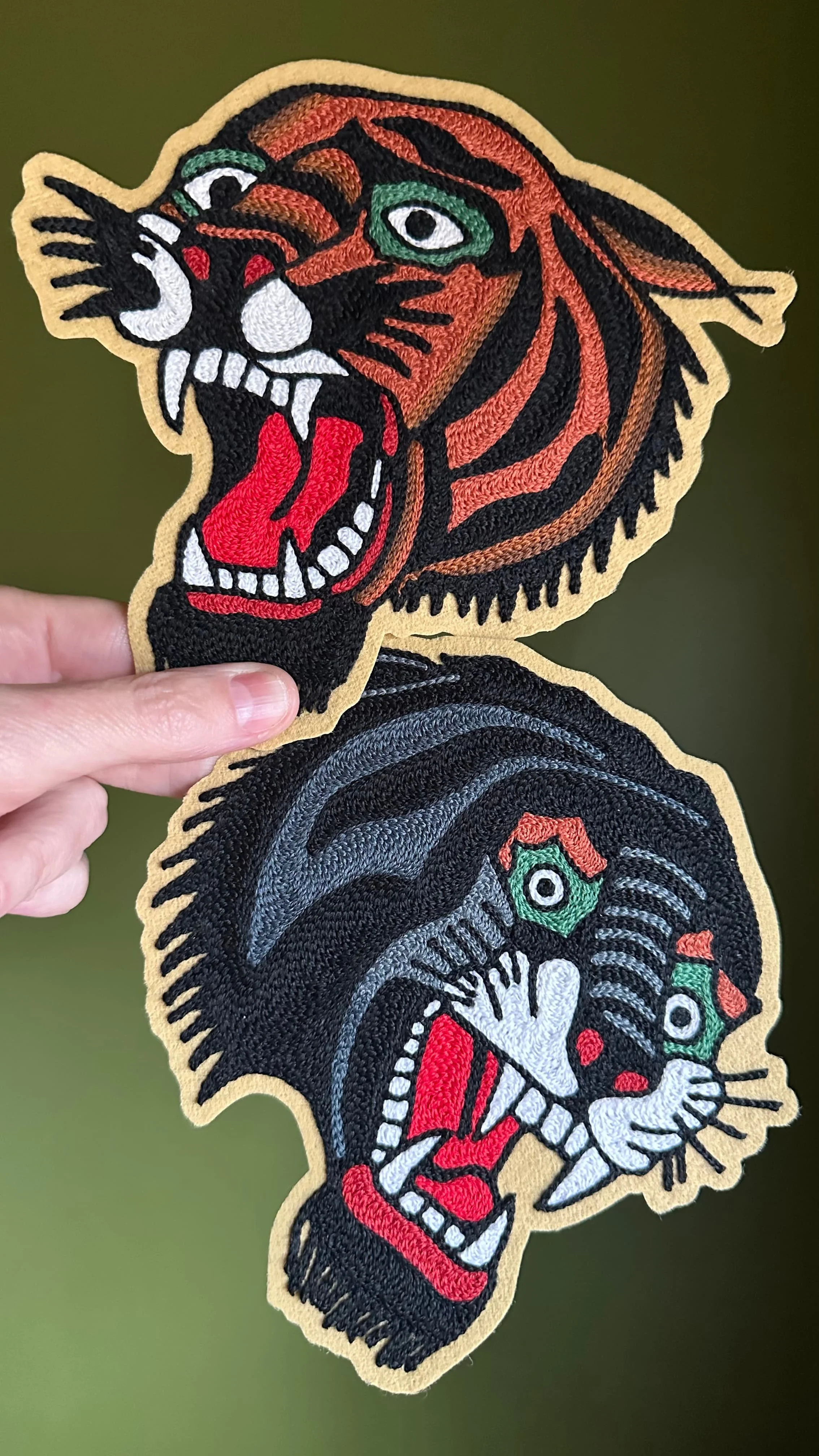 Close-up of an embroidered patch featuring a roaring tiger with orange and black stripes, green eyes, and a red tongue, against a dark background.