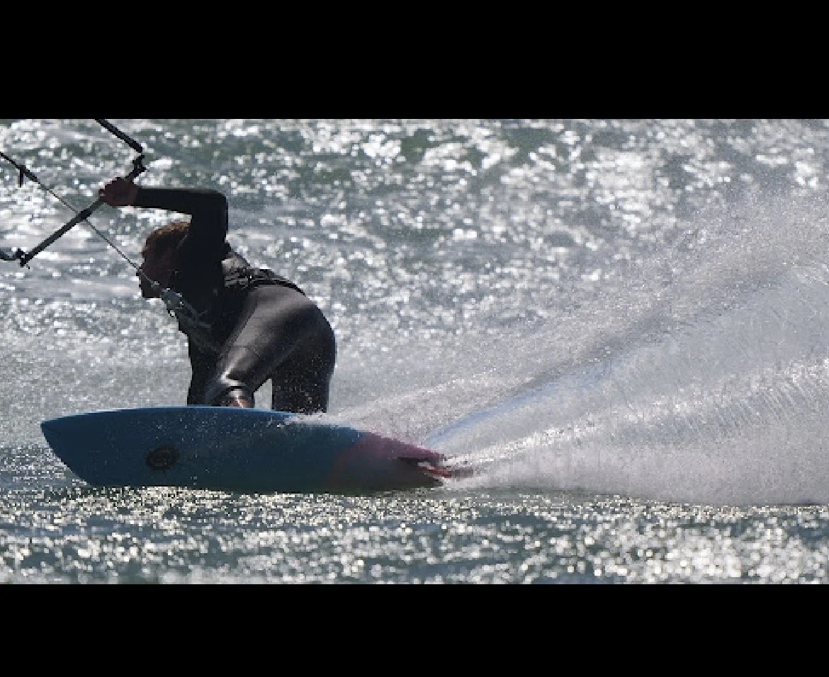 Person kite surfing on the water, holding onto the kite control bar and leaning back.