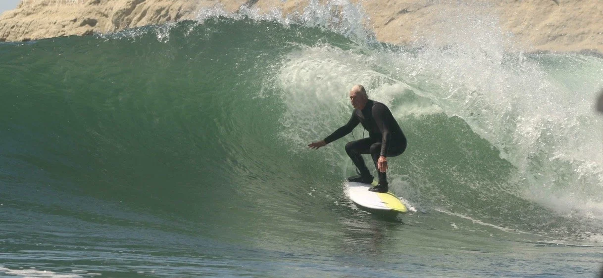 A man wearing a wetsuit surfing on a yellow surfboard inside a large wave.