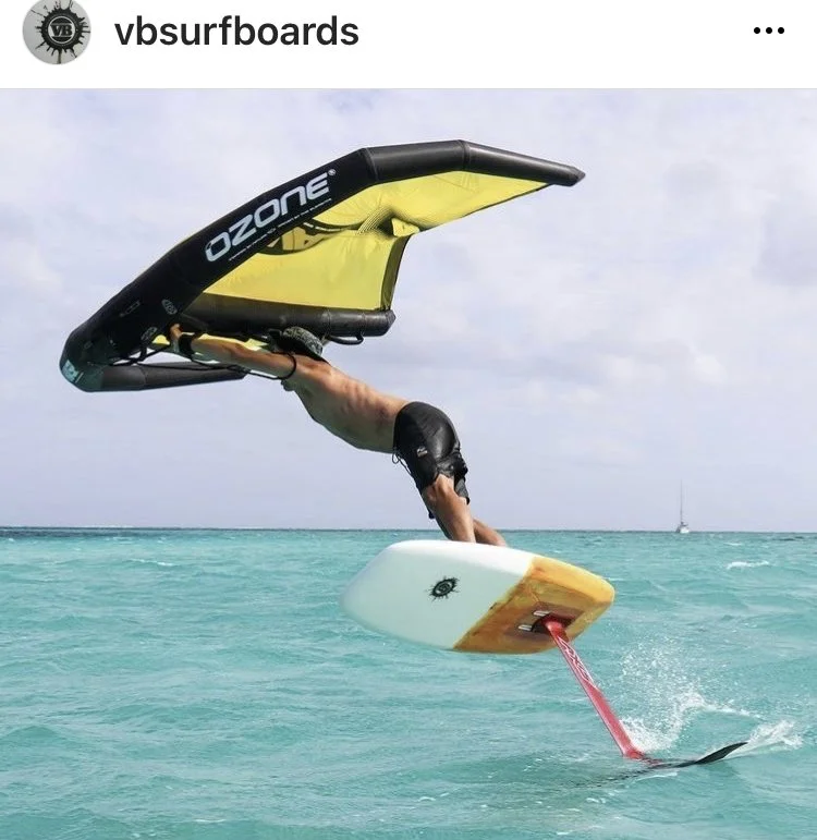 Person performing a skillful water stunt with a surfboard and a stand-up paddleboard on turquoise ocean.