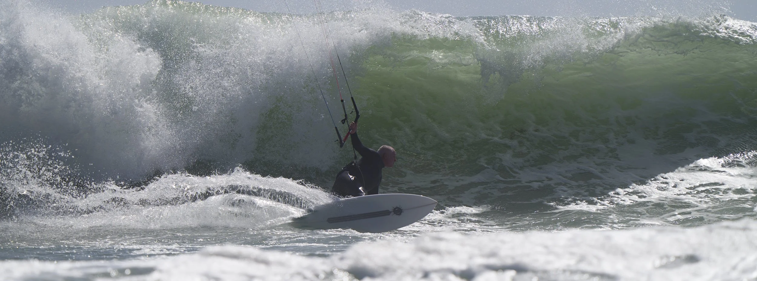 A person kiteboarding on the ocean with large waves crashing around him.