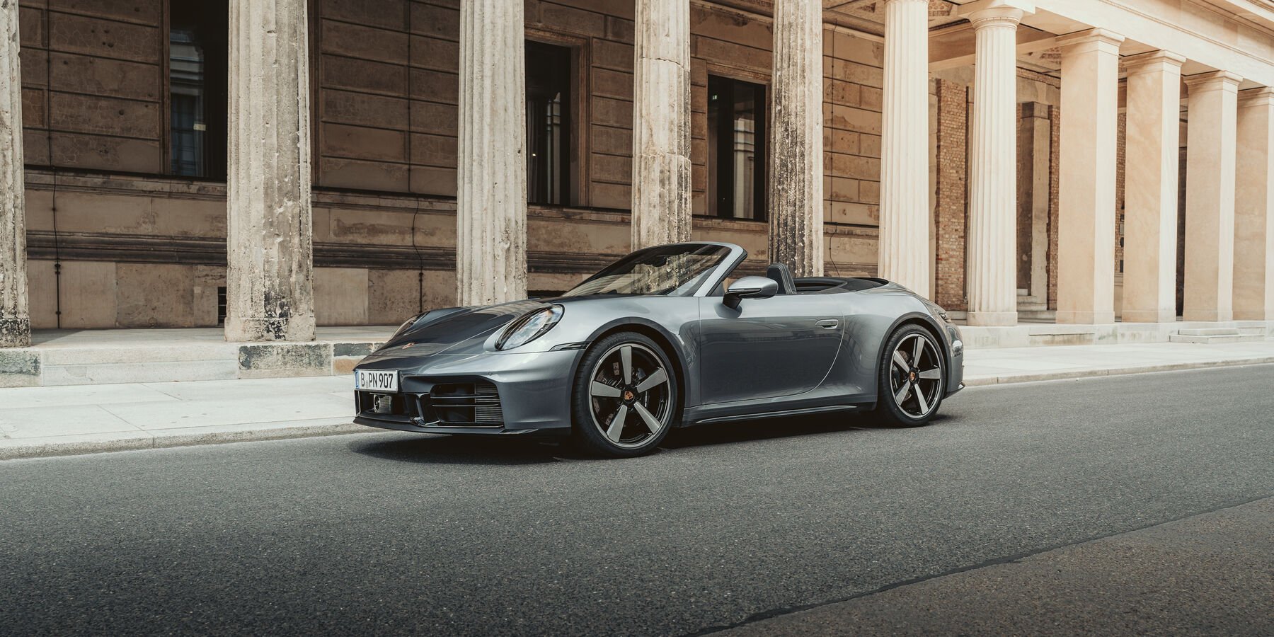 Silberner Porsche 911 Cabriolet parkend an einer Straßenseite vor einer alten, historischen Gebäudefassade mit großen Säulen.