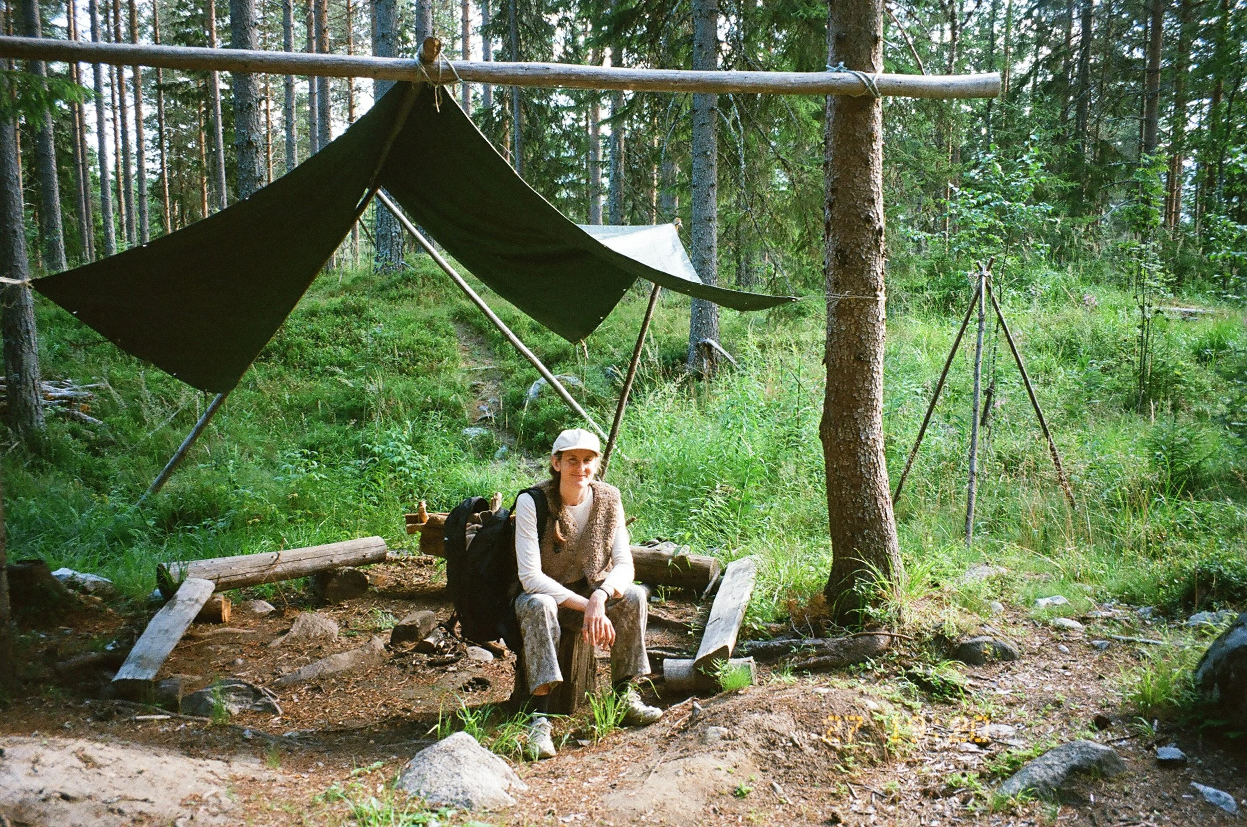 Danielle Davis sitting beside a hearth under a forest shelter.