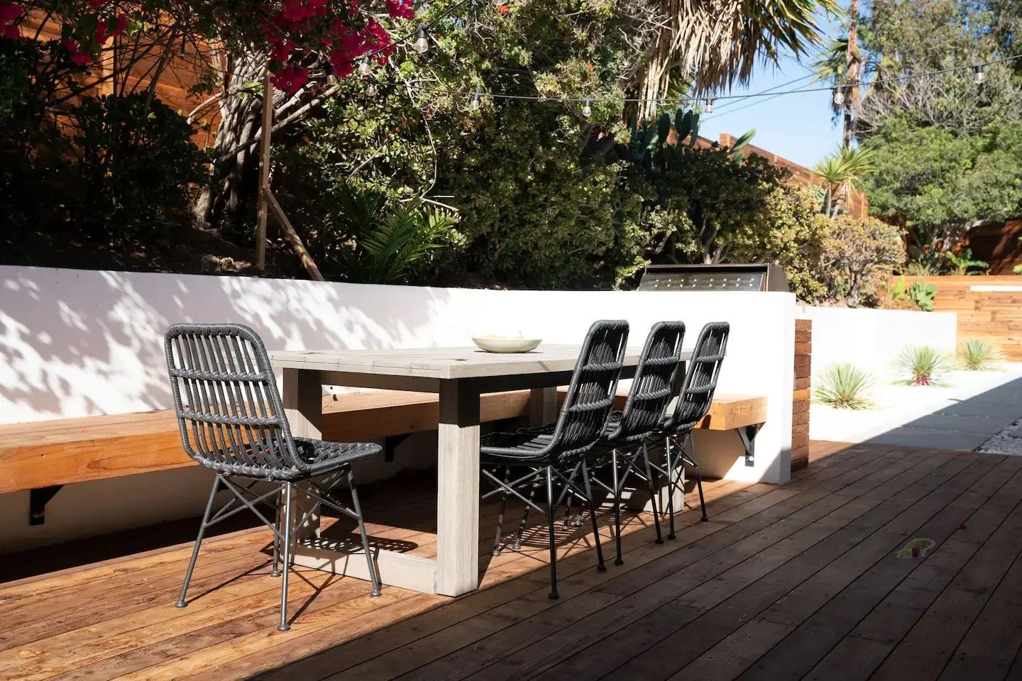 Modern outdoor dining area with a custom wood deck, built-in seating, barbecue, and tropical landscape design in Malibu, California.