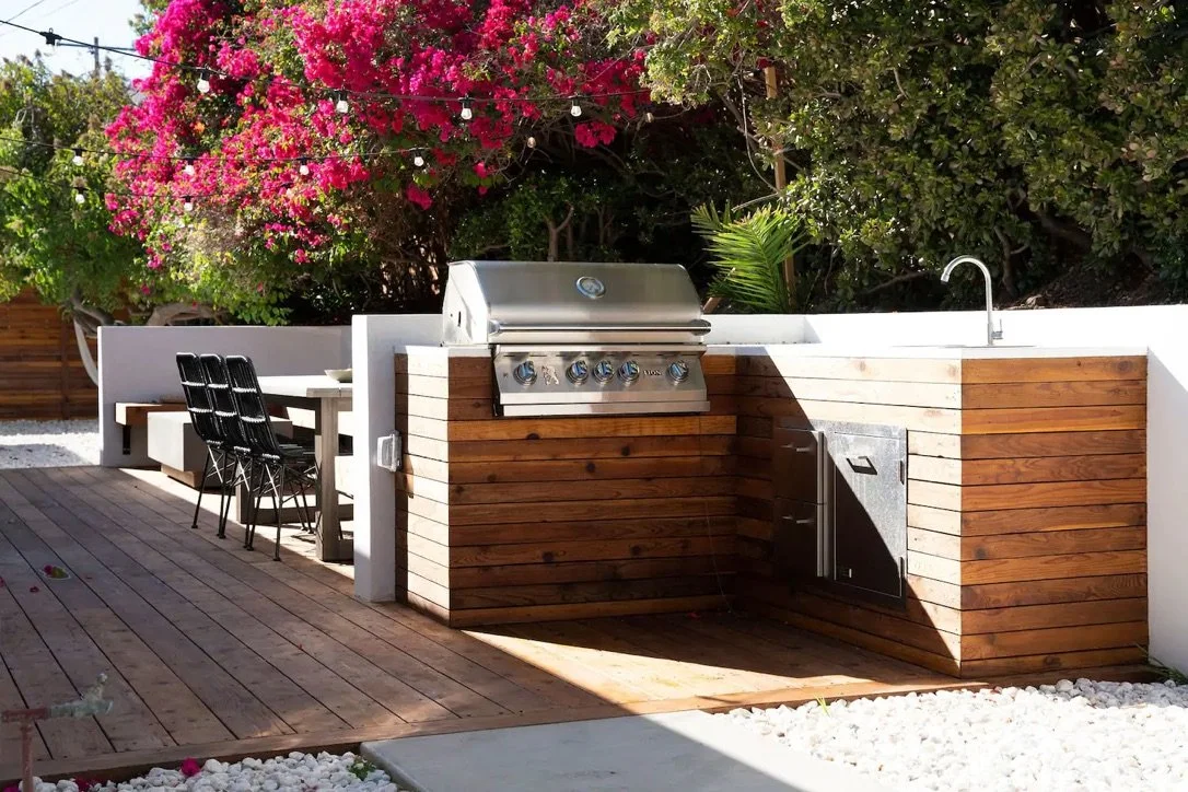 Custom redwood outdoor kitchen with built-in BBQ grill, sink, outdoor dining area, and modern Malibu landscape design.