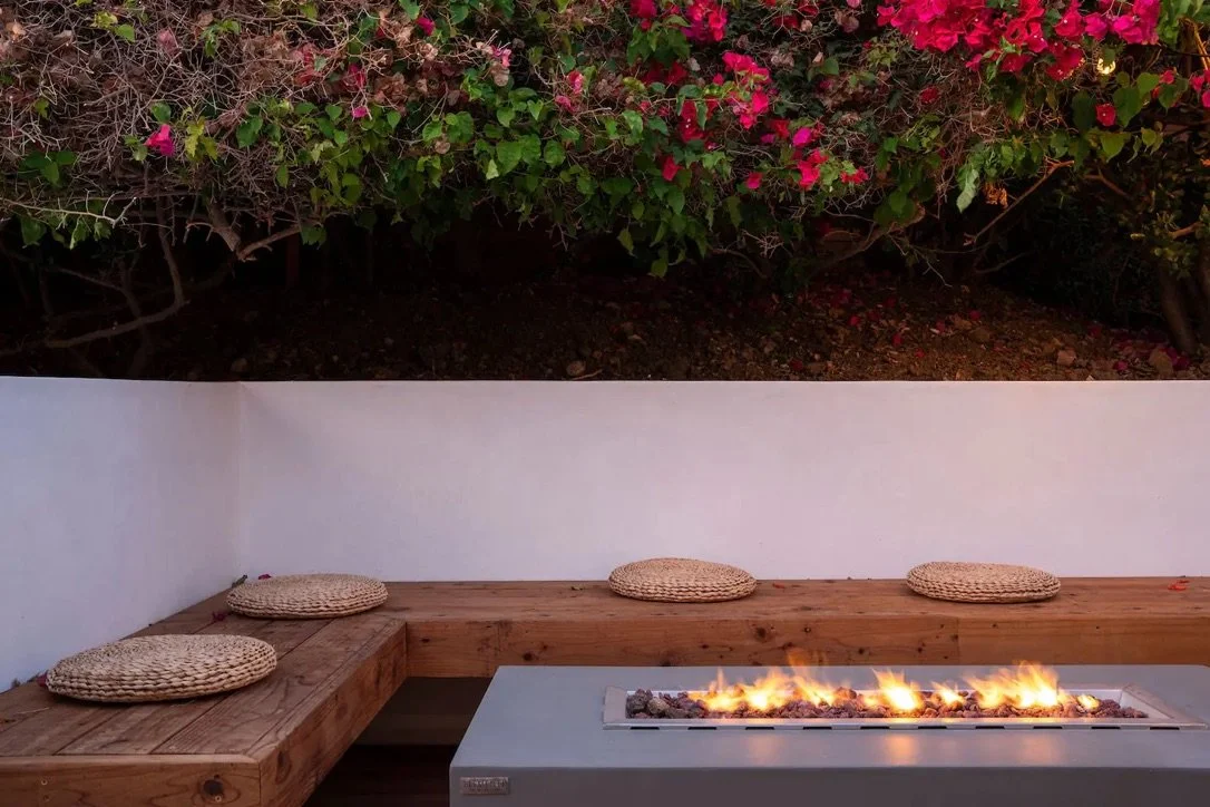 Evening outdoor living design in Malibu with a contemporary fire pit, custom bench seating, wood deck, and flowering bougainvillea.